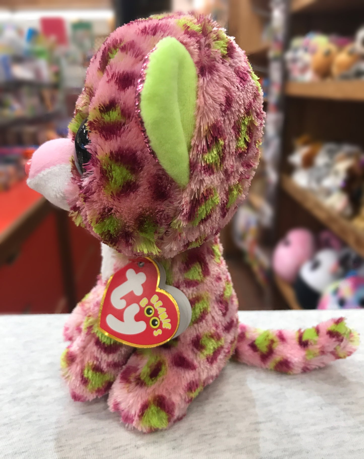 Ty Beanie Boo Lainey plush leopard with pink and green fur, sitting on display in toy store with heart-shaped tag
