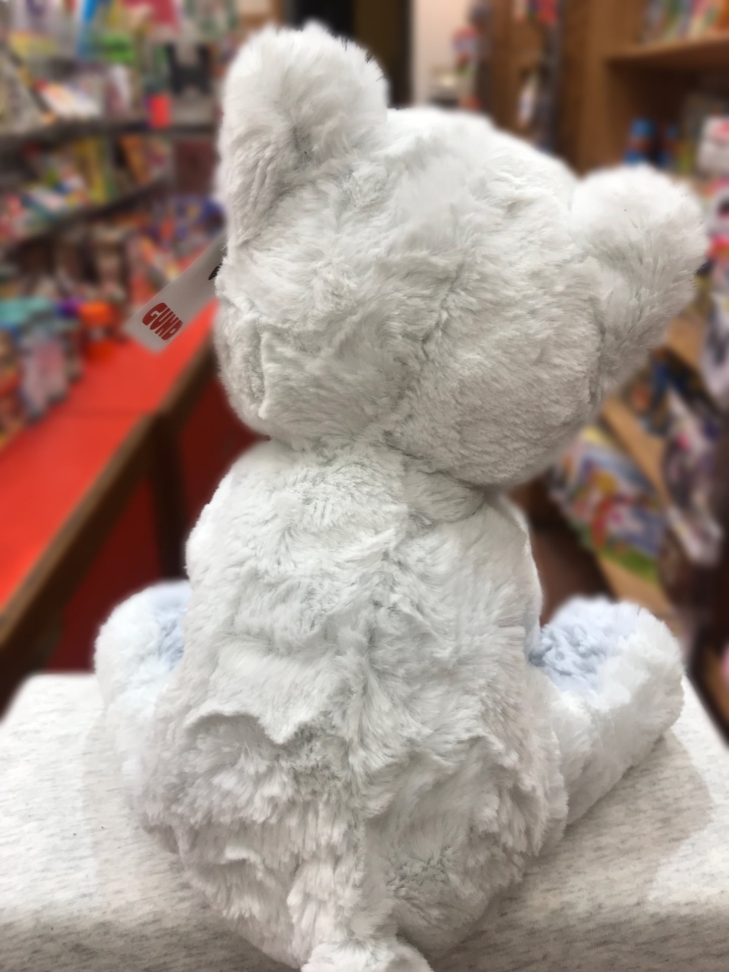 Soft white Gund Cozys Kitty Cat plush toy, 10 inches long, sitting on display in a store with floppy ears and limbs