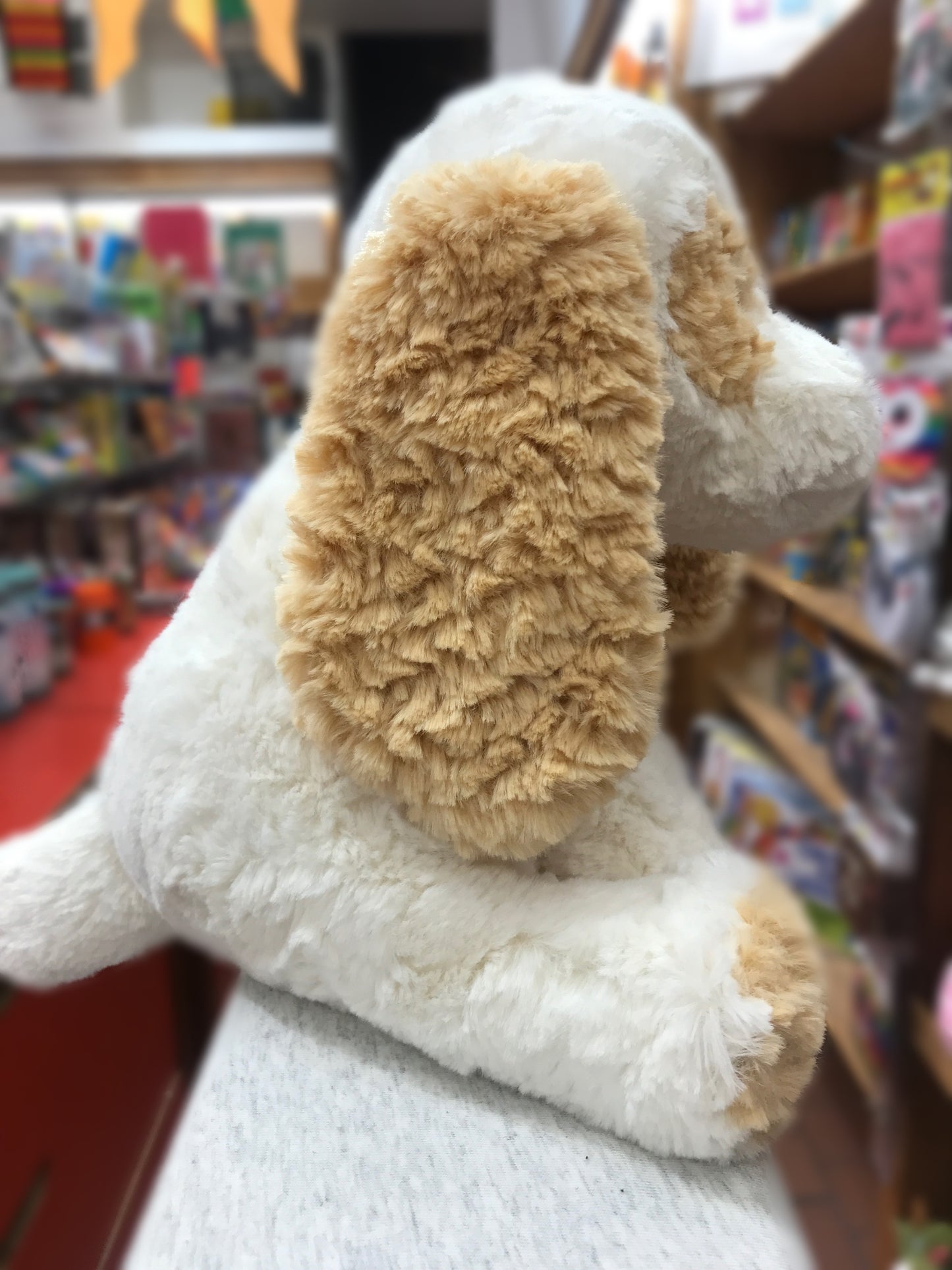 Soft Gund Cozys puppy plush toy with cream and tan fur, floppy ear visible, in a bookstore setting