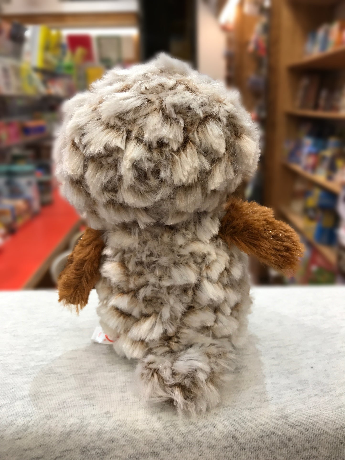 Ty Beanie Boo Percy barn owl plush toy with fluffy brown-tipped feathers, shown from behind in a store setting