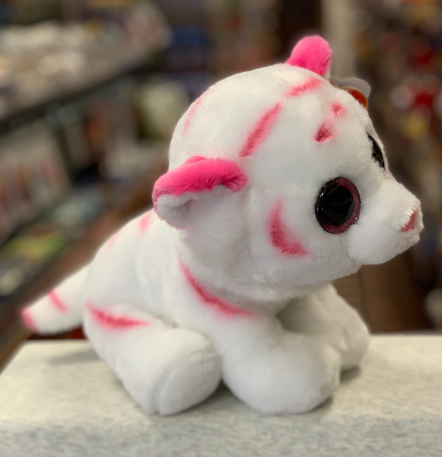 Fluffy white Ty Beanie Baby tiger plush with pink stripes and large eyes, sitting on display in a toy store