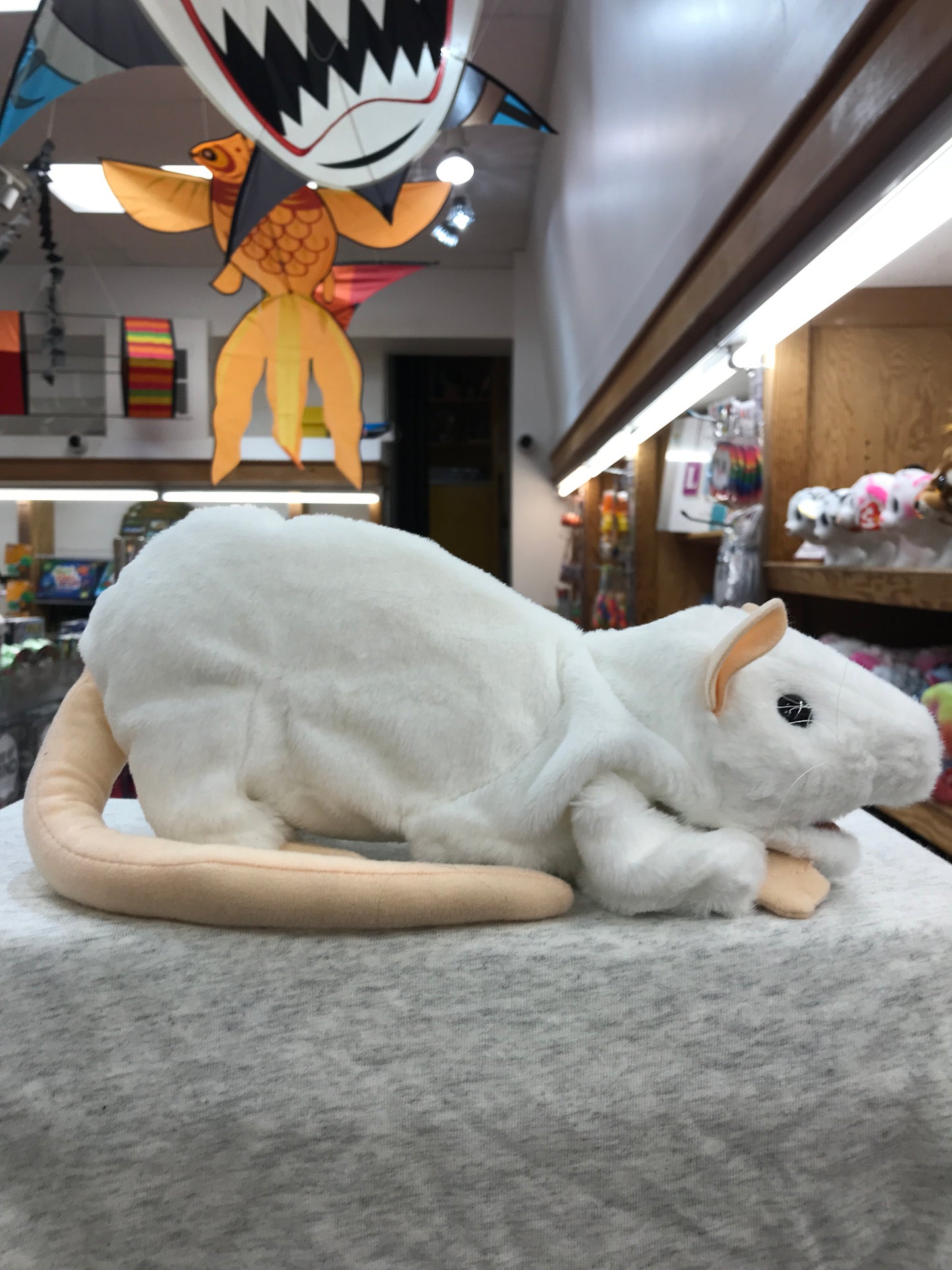 White rat puppet sitting in toy store, with movable mouth and arms, colorful decorations visible in background
