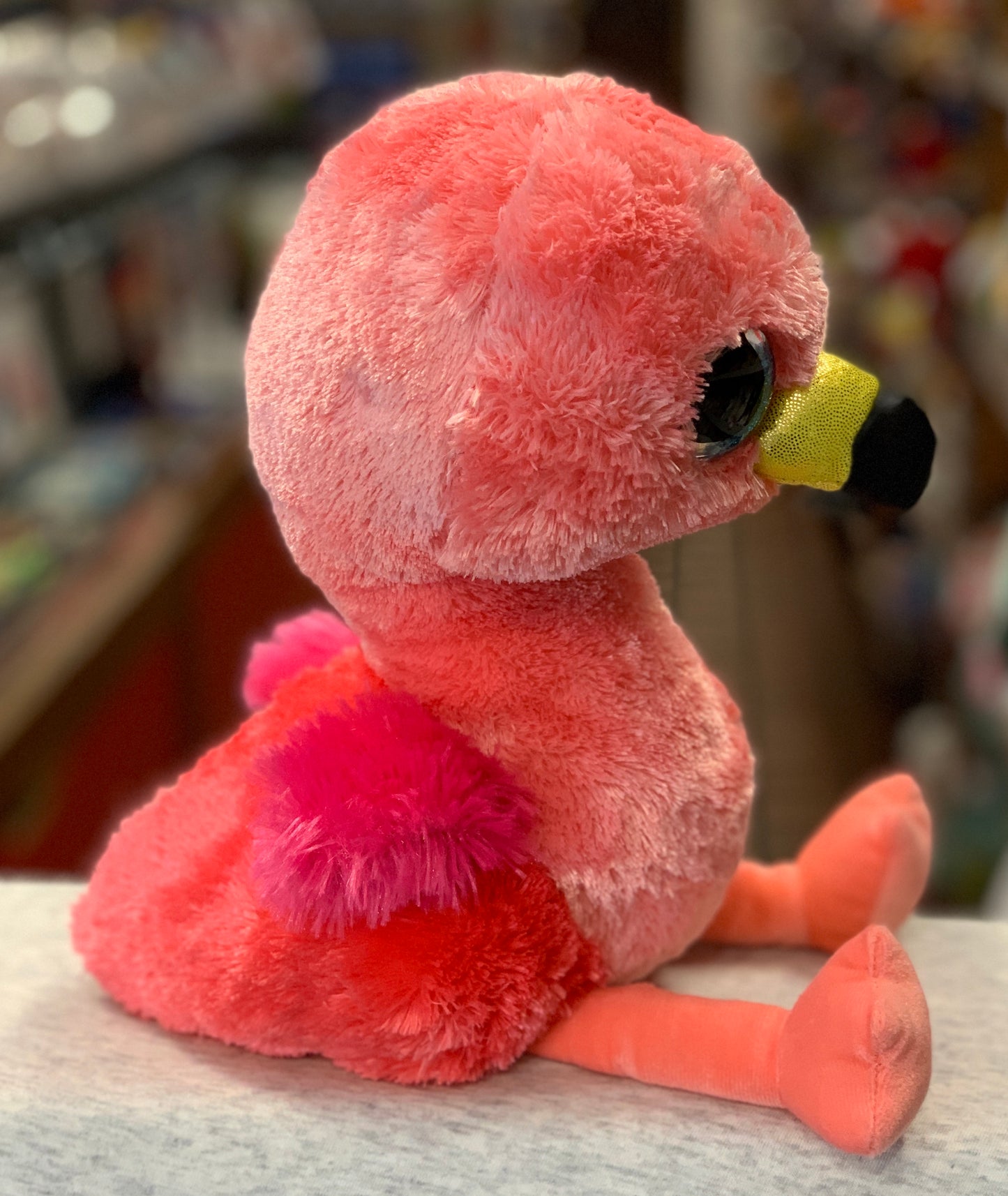 Adorable pink Ty Beanie Boo Gilda Flamingo plush toy with large sparkly eyes and yellow beak, sitting on display shelf