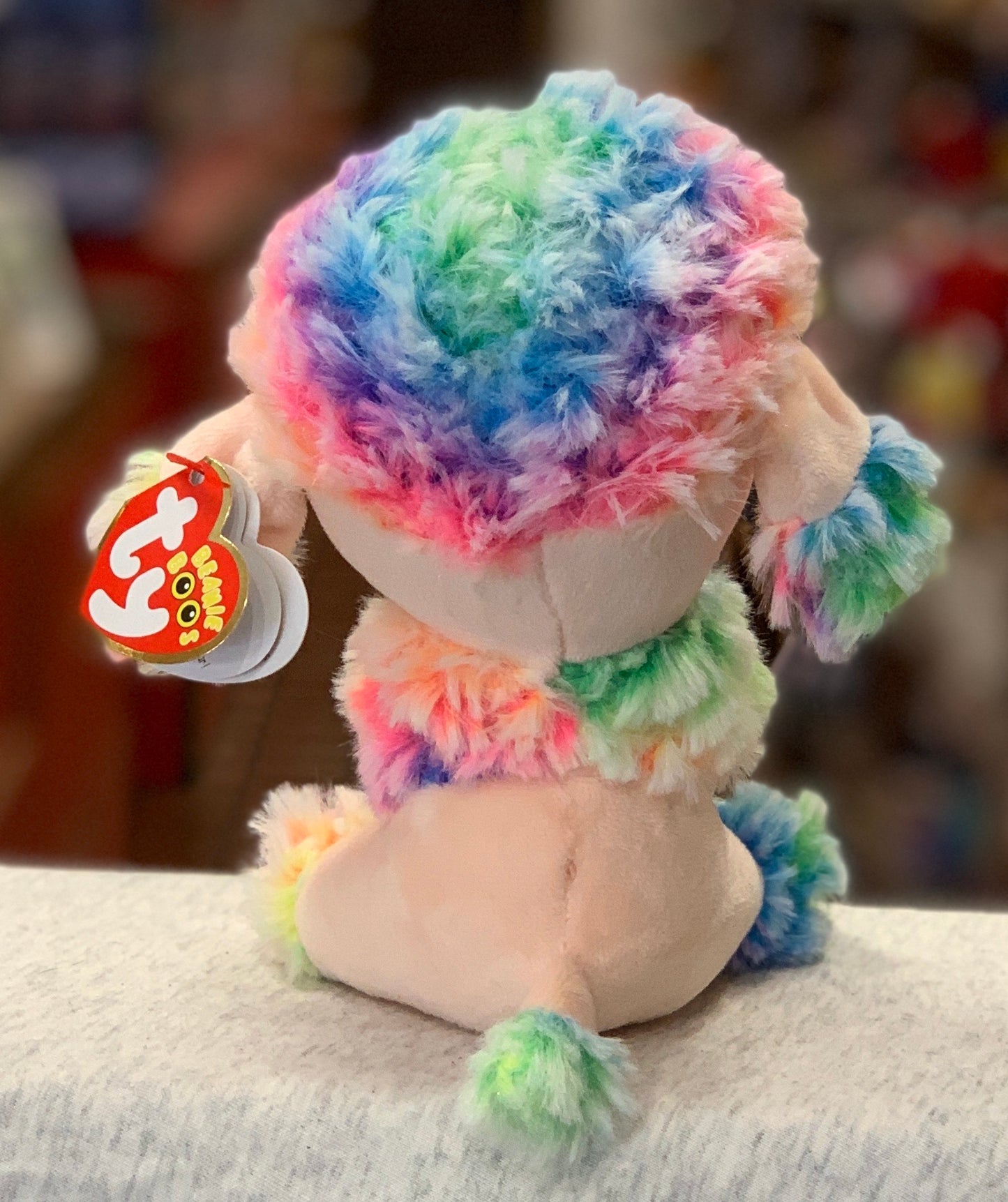 Ty Beanie Boo Rainbow poodle plush with colorful fur, shown from behind with tag visible, soft and cuddly collectible toy