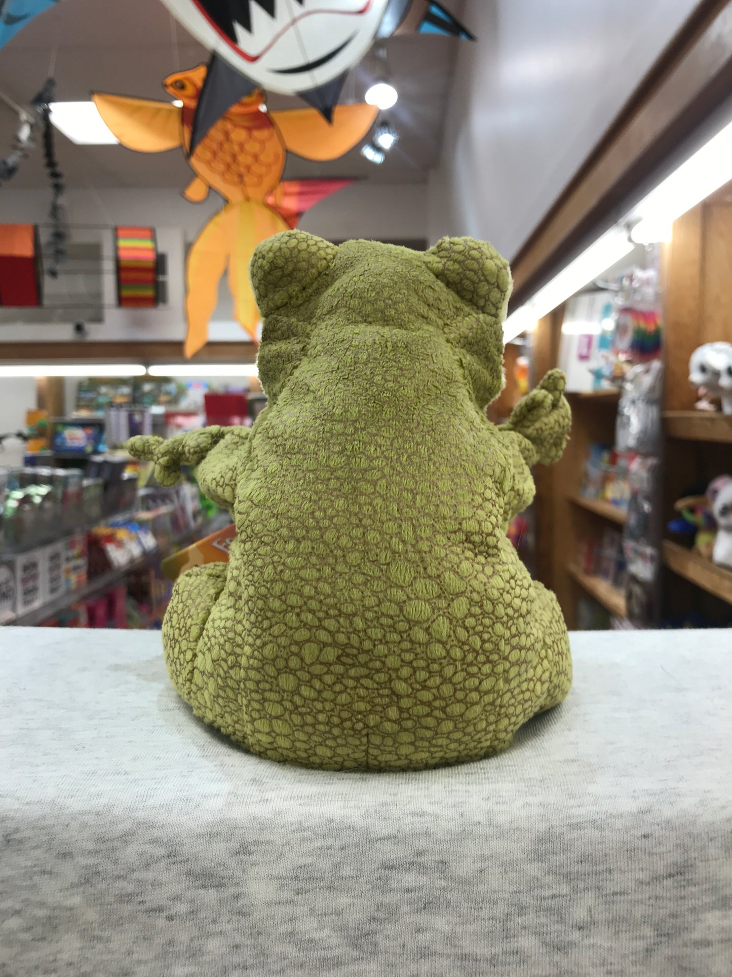 Folkmanis Funny Frog Puppet in chartreuse, textured fabric sitting on display in toy store, viewed from behind