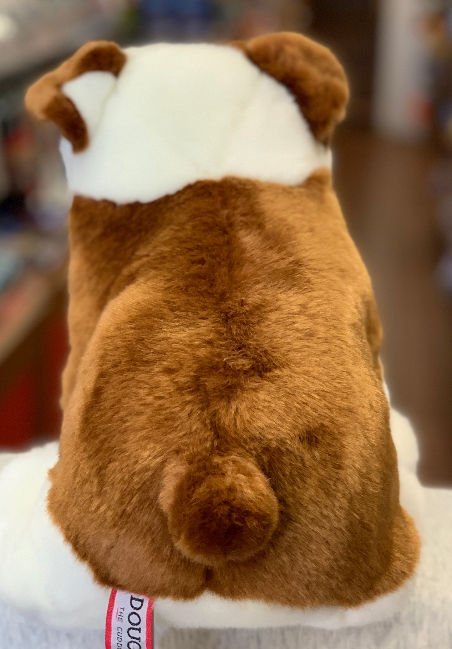 Plush bulldog stuffed animal with brown and white fur, viewed from behind, showing realistic wrinkles and tail