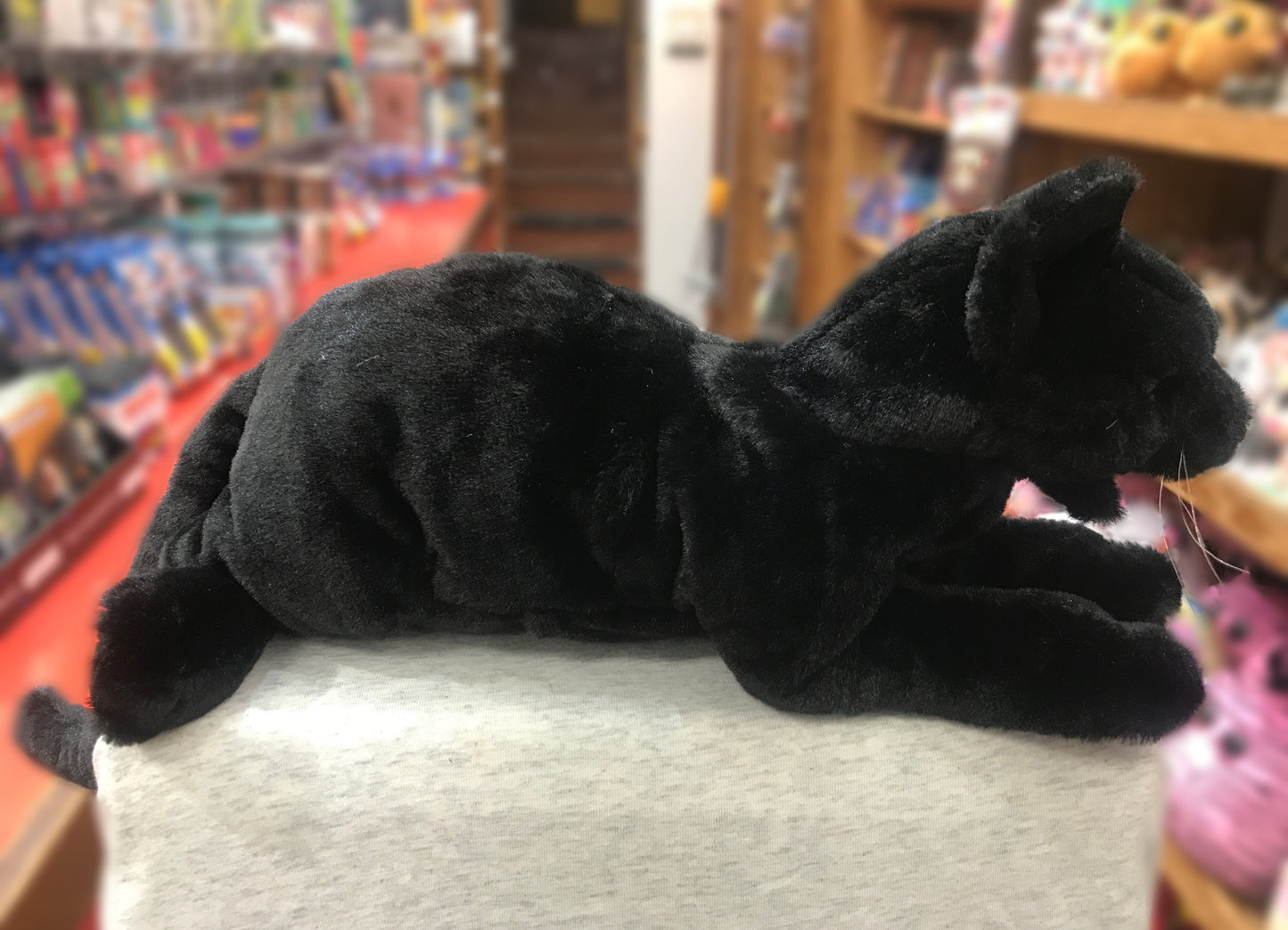 Folkmanis Black Cat Puppet with sleek ebony plush, stretched out and ready for play, in toy store setting