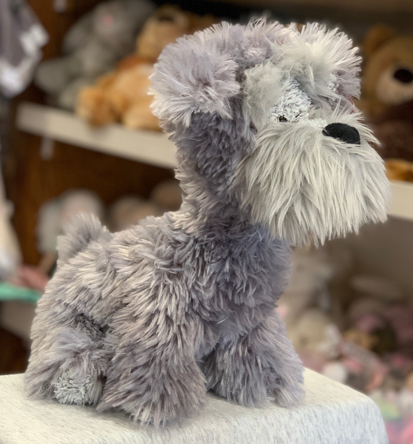 Gund Bentley wire hair terrier plush toy, gray and white, sitting on display with other stuffed animals in background