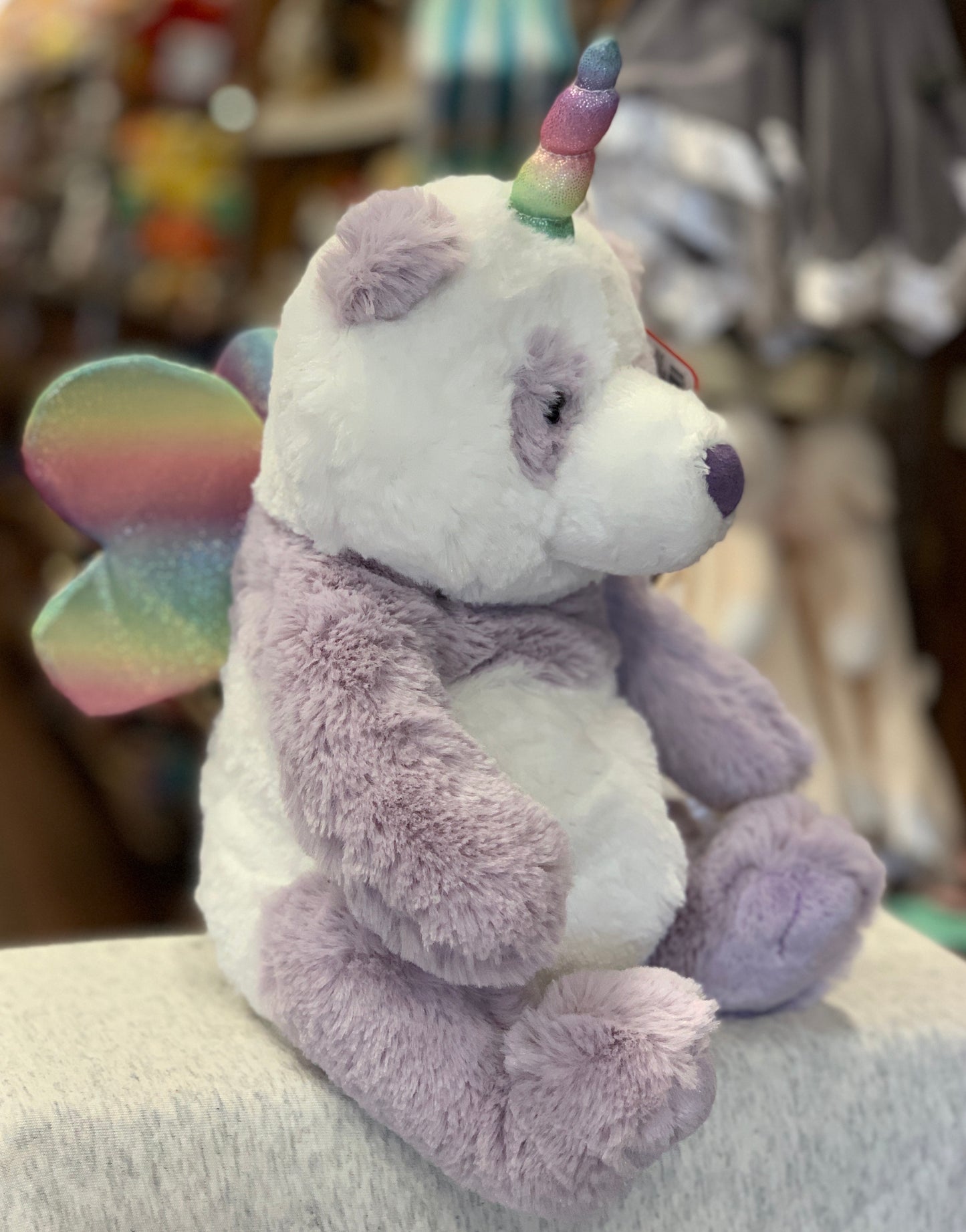 Gund Pandacorn plush toy with rainbow horn, iridescent wings, and purple-white fur, sitting on display in store