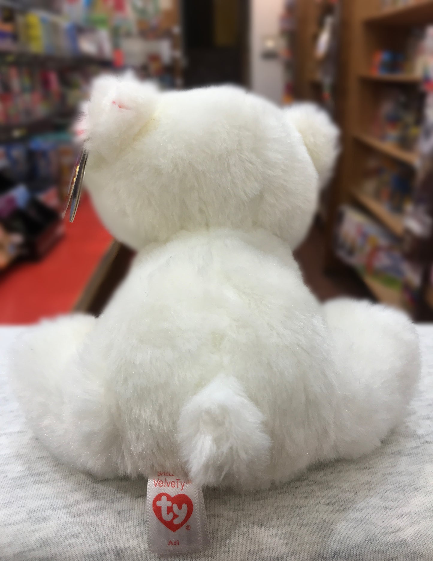 Ty Beanie Baby Ari white polar bear plush toy, soft and fluffy, shown from behind with tag visible in toy store setting