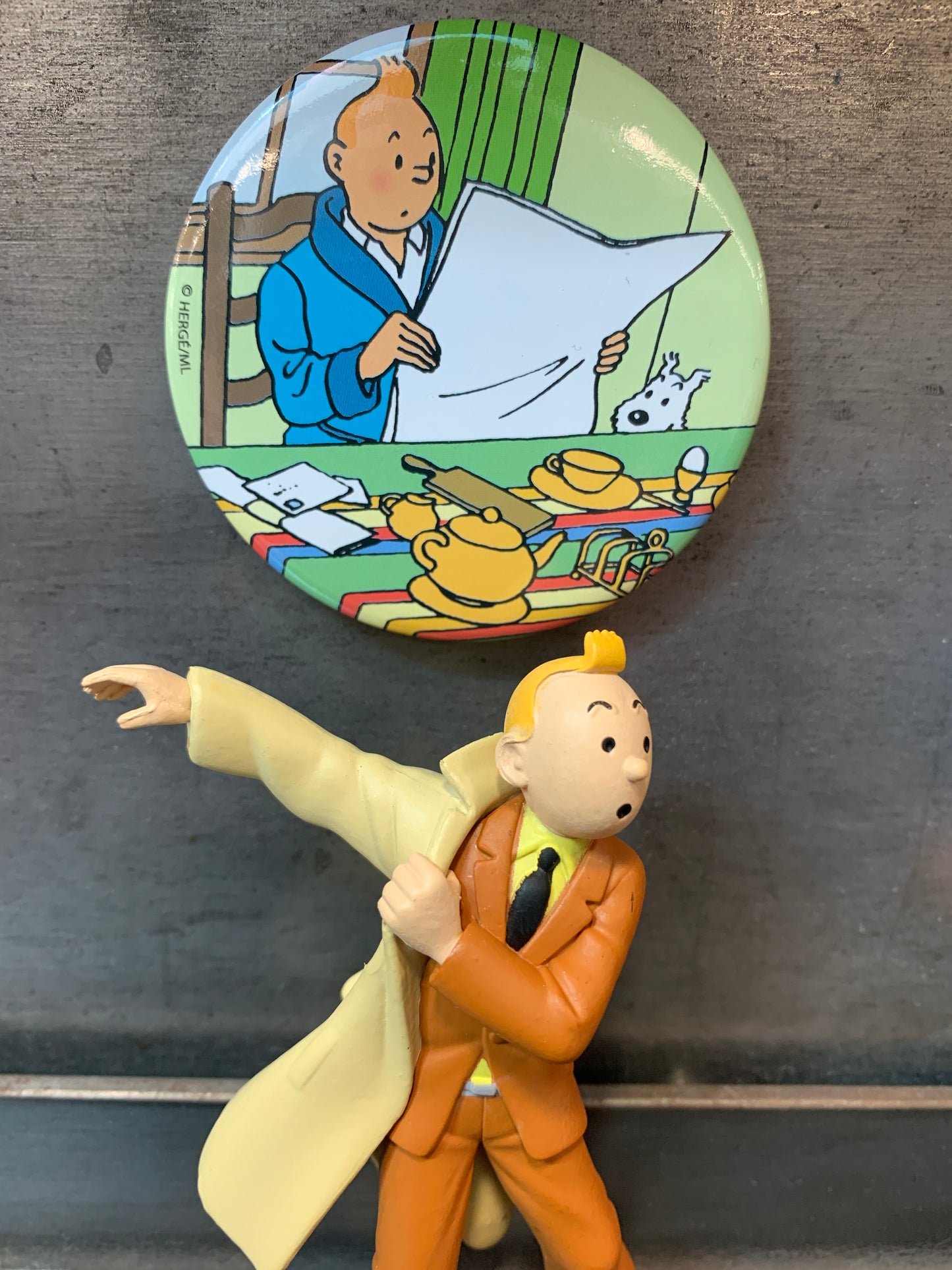 Tintin reading newspaper magnet with Snowy, displayed above character figurine in trench coat