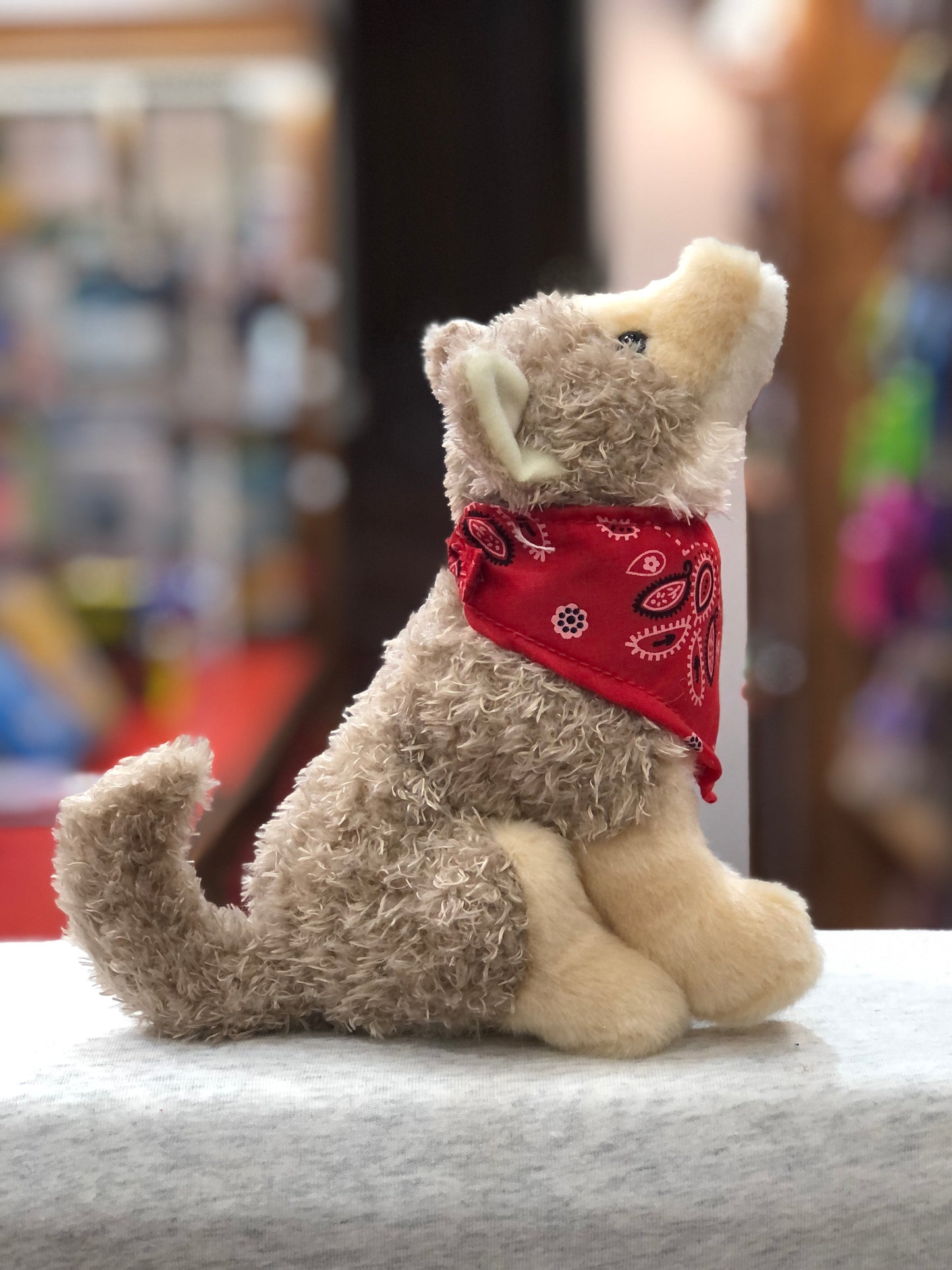 Plush coyote stuffed animal with red bandana howling, seated on display in toy store