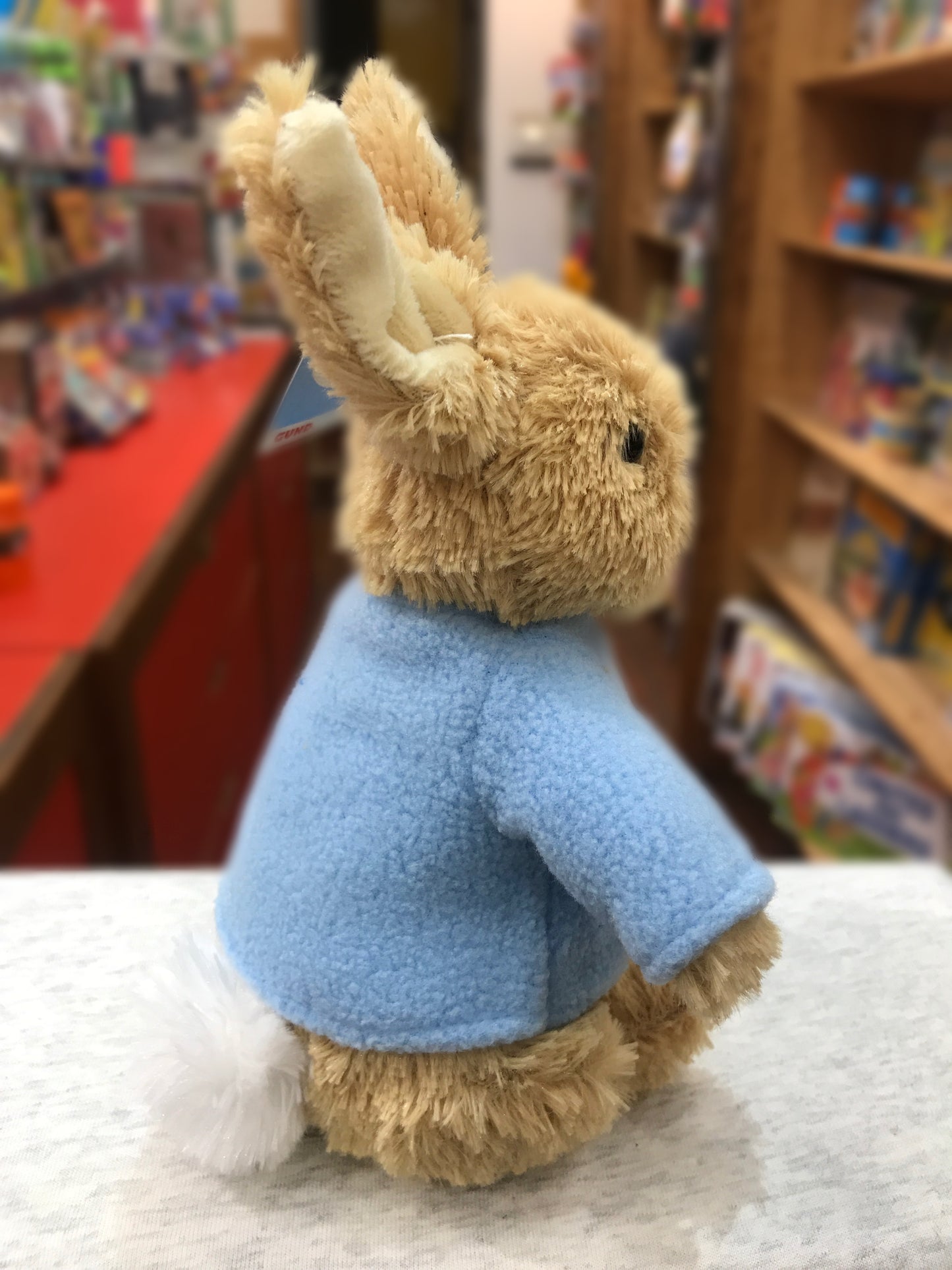 Gund Peter Rabbit plush toy with light blue coat, sitting in bookstore, faithful recreation of Beatrix Potter character