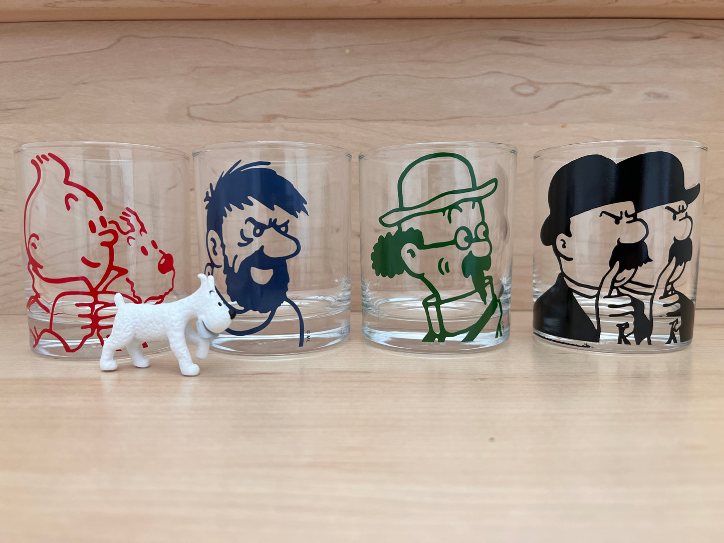 Tintin character glass tumblers set featuring colorful designs of four iconic figures, with small white dog figurine