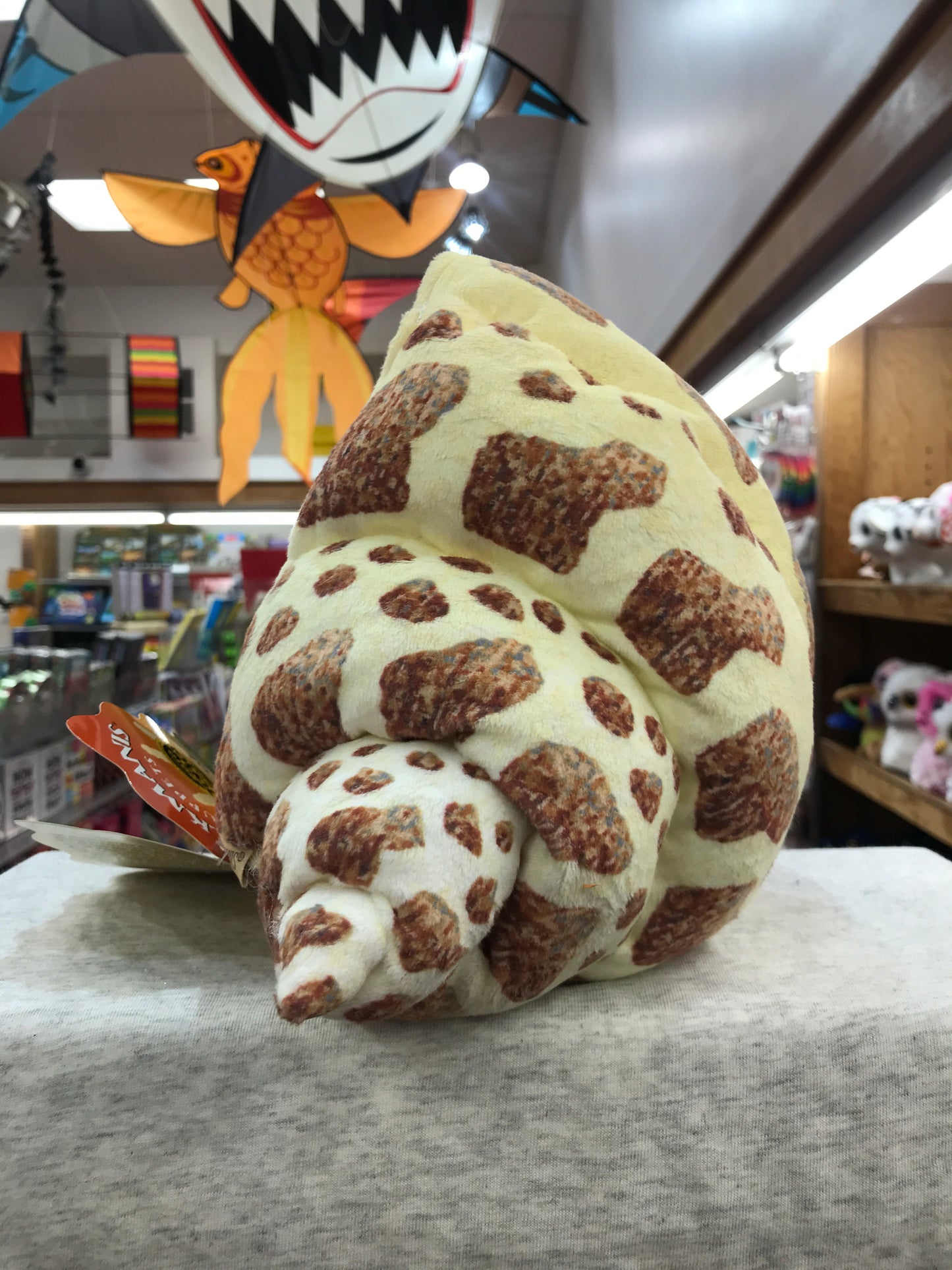 Folkmanis hermit crab puppet with patterned shell in toy store, colorful hanging decorations visible in background