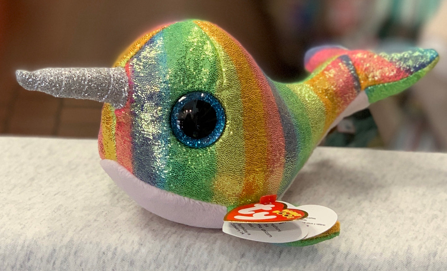 Colorful Ty Beanie Boo Nori Narwhal plush toy with sparkly rainbow body, large blue eyes, and silver horn on white surface