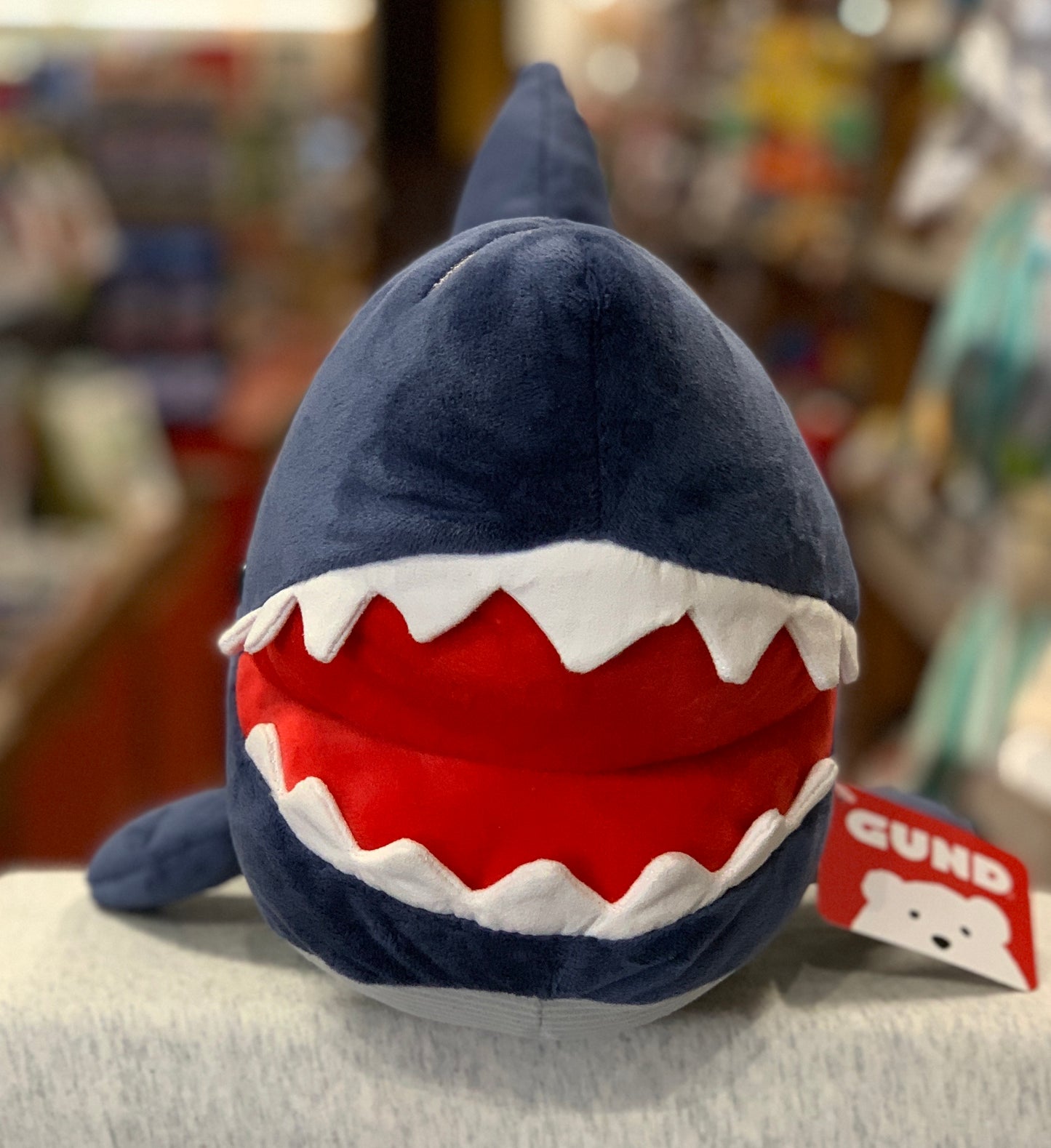 Gund Maxwell Shark plush toy with open mouth, showing red interior and white teeth, on display in store