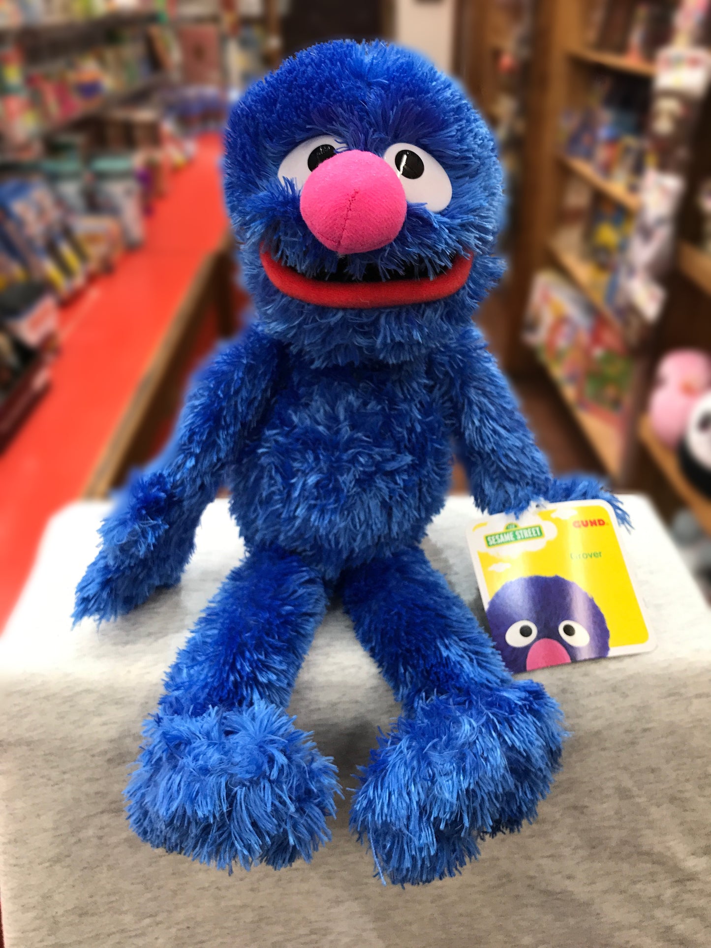 GUND Sesame Street Grover plush toy, 14.5 inches tall, blue furry body, pink nose, sitting on display in store