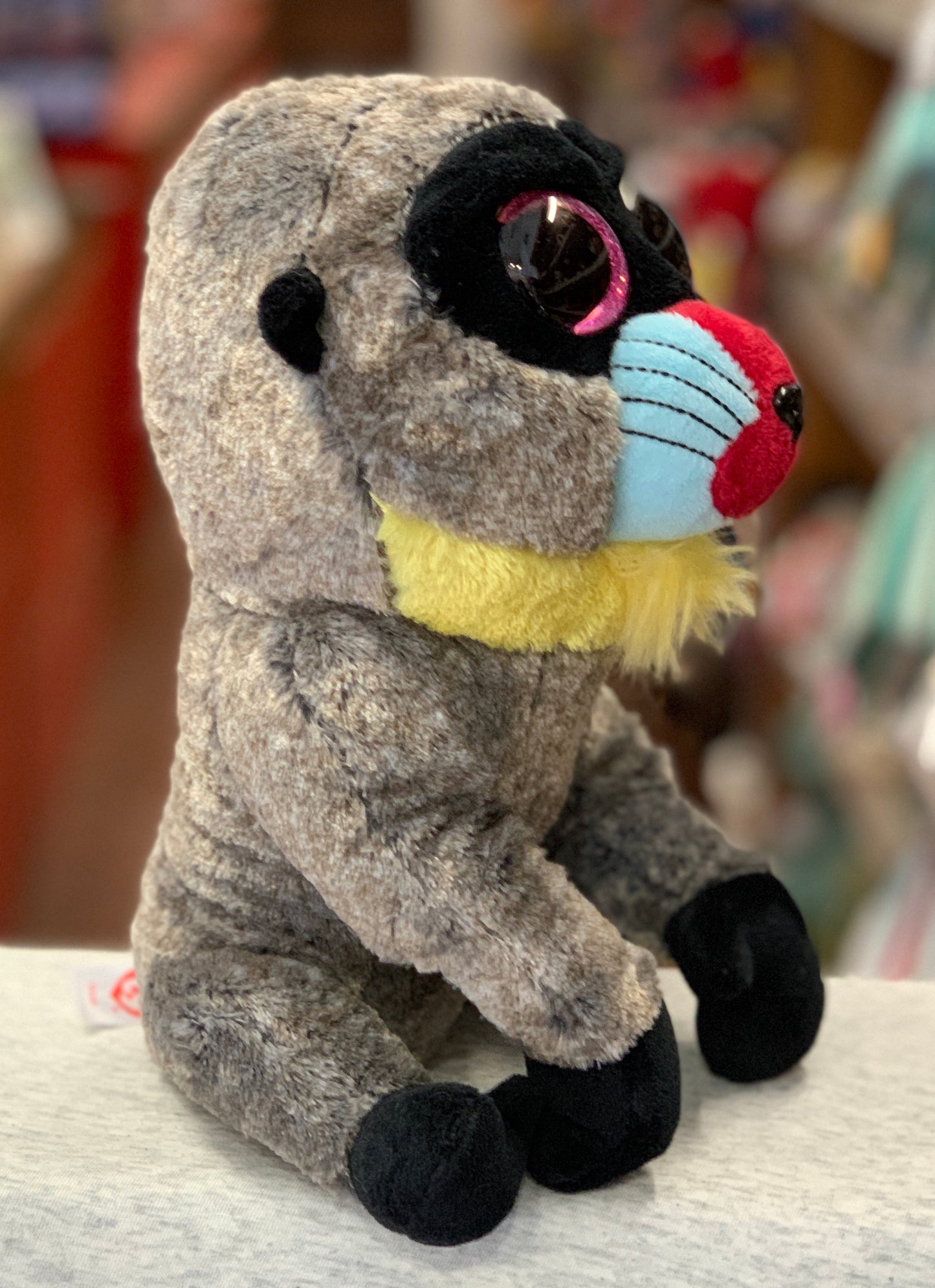 Ty Beanie Boo Wasabi Baboon plush toy with colorful face, large sparkly eyes, and soft gray fur, sitting on display