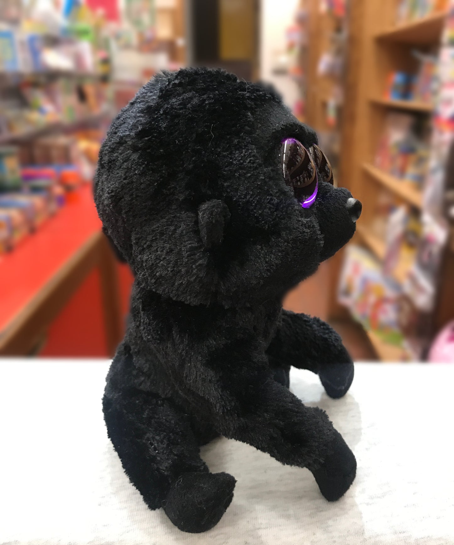 TY Beanie Boo George Gorilla plush toy with purple glittery eyes, sitting on display in a colorful toy store