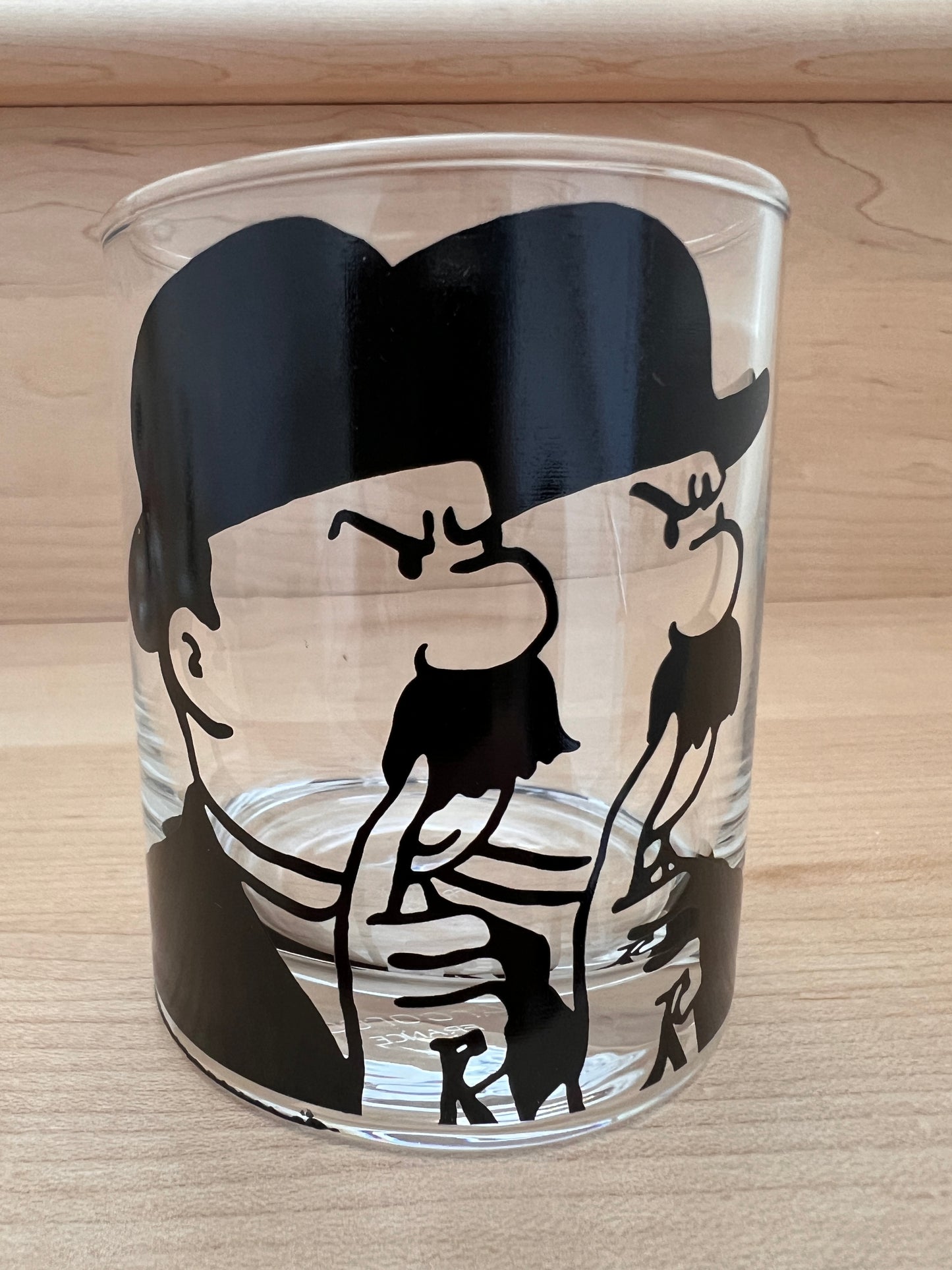 Glass tumbler from Tintin collectible set featuring silhouette design of Thomson and Thompson characters on clear glass
