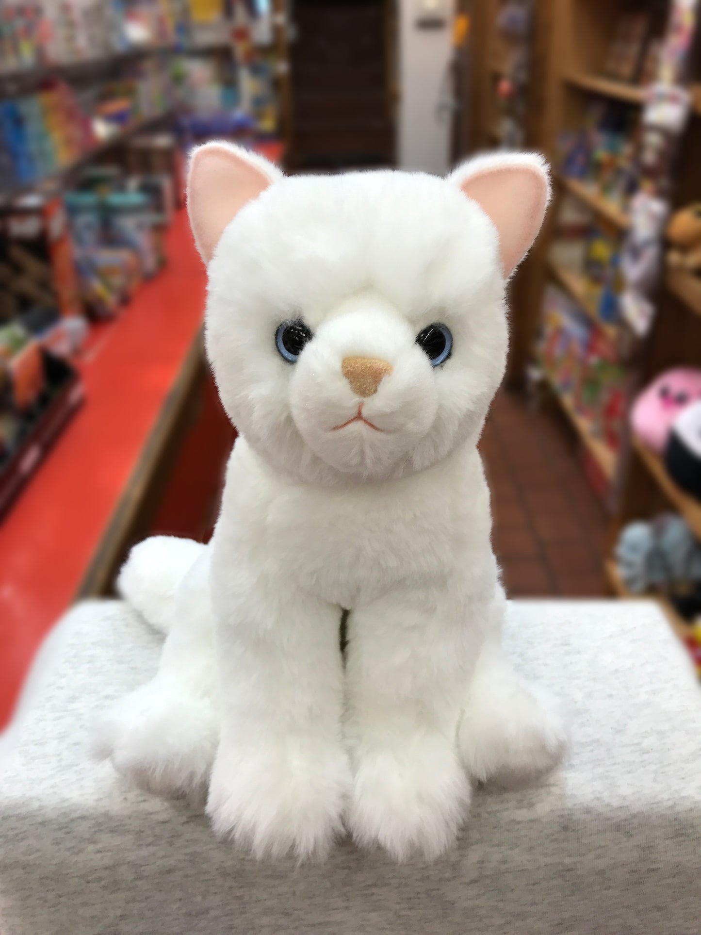 Soft white cat plush toy with blue eyes sitting on display in toy store, cuddly Winnie stuffed animal for children