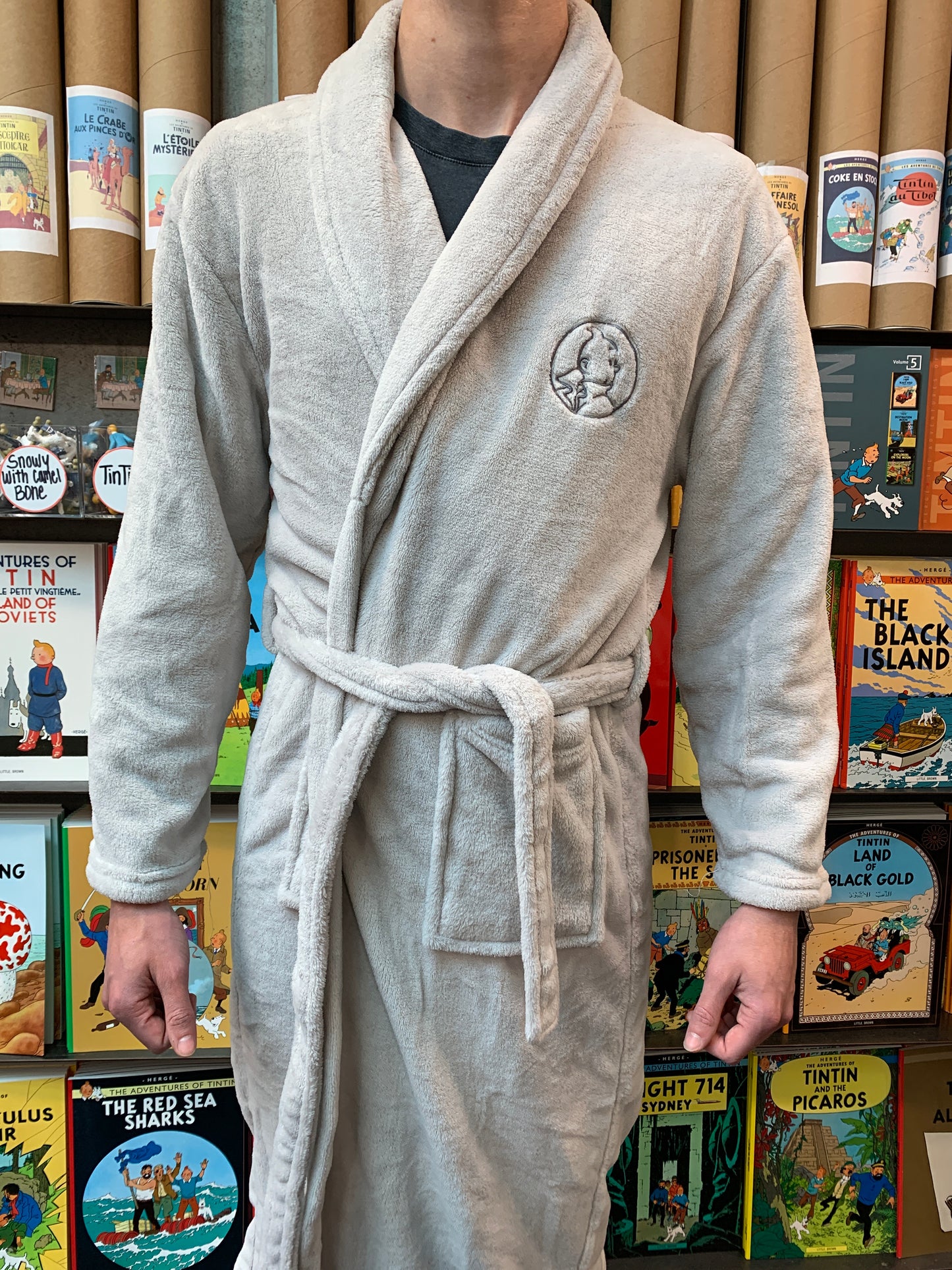 Plush grey Tintin robe with embroidered logo, shown against colorful Tintin book covers, perfect for cozy reading