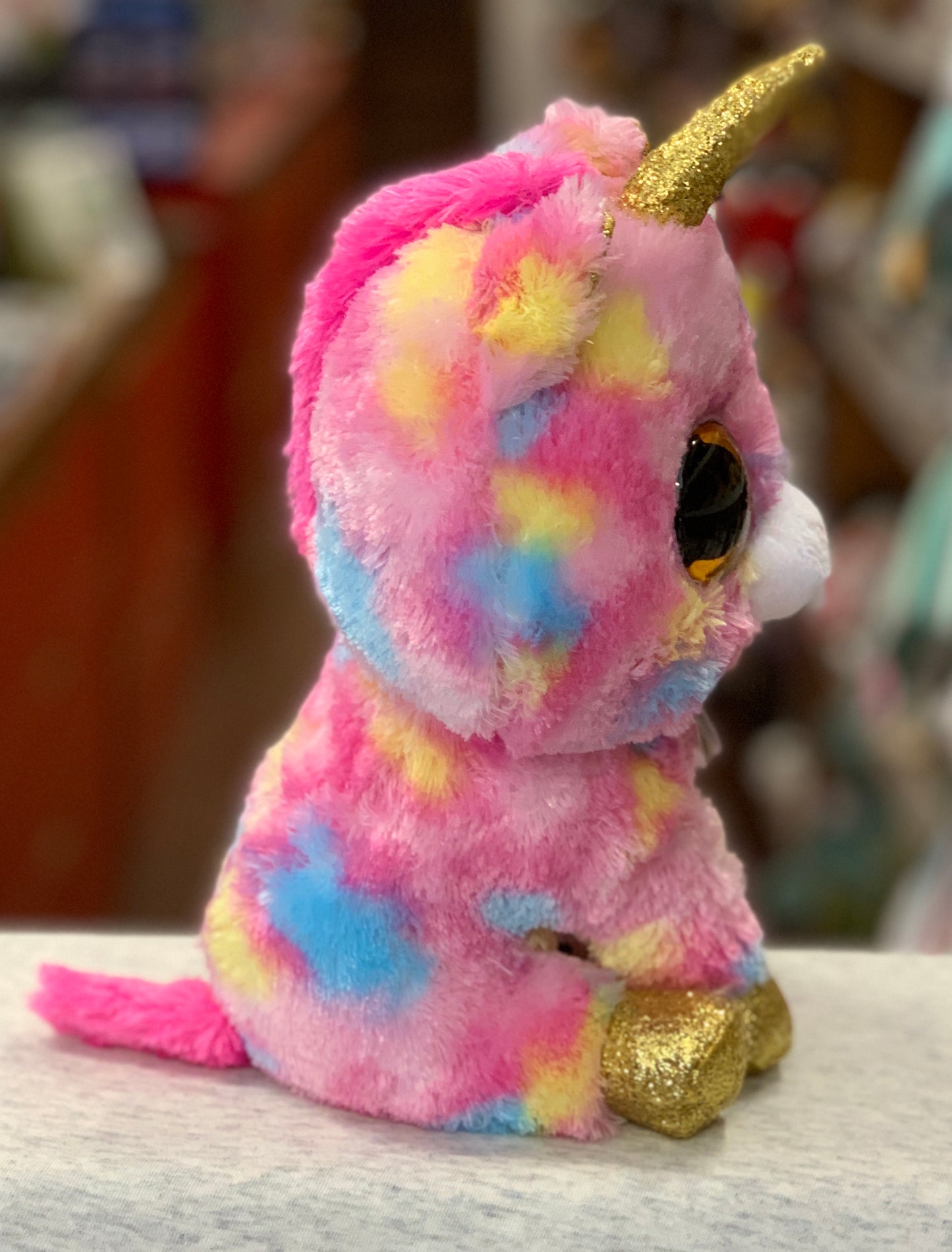 Colorful Ty Beanie Boo Fantasia unicorn plush toy with pink, blue, and yellow fur, gold horn and hooves, and large sparkly eyes