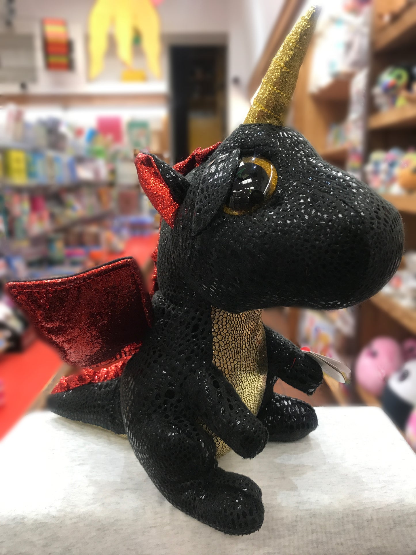 Ty Beanie Boo Grindal dragon plush with glittery gold horn, red wings, and golden eyes, displayed in toy store setting
