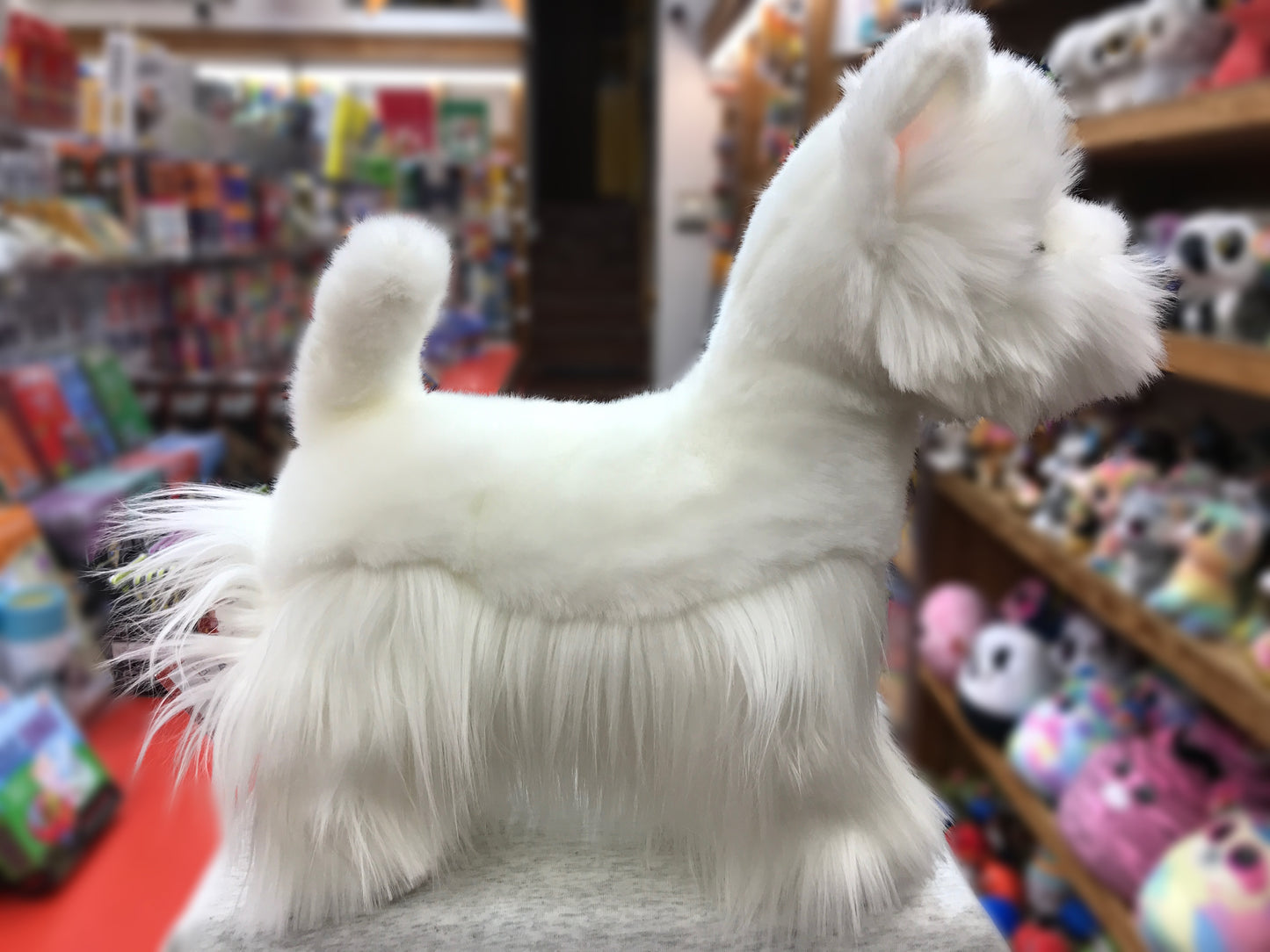 Realistic plush West Highland White Terrier dog in toy store, showcasing soft white fur and alert pose