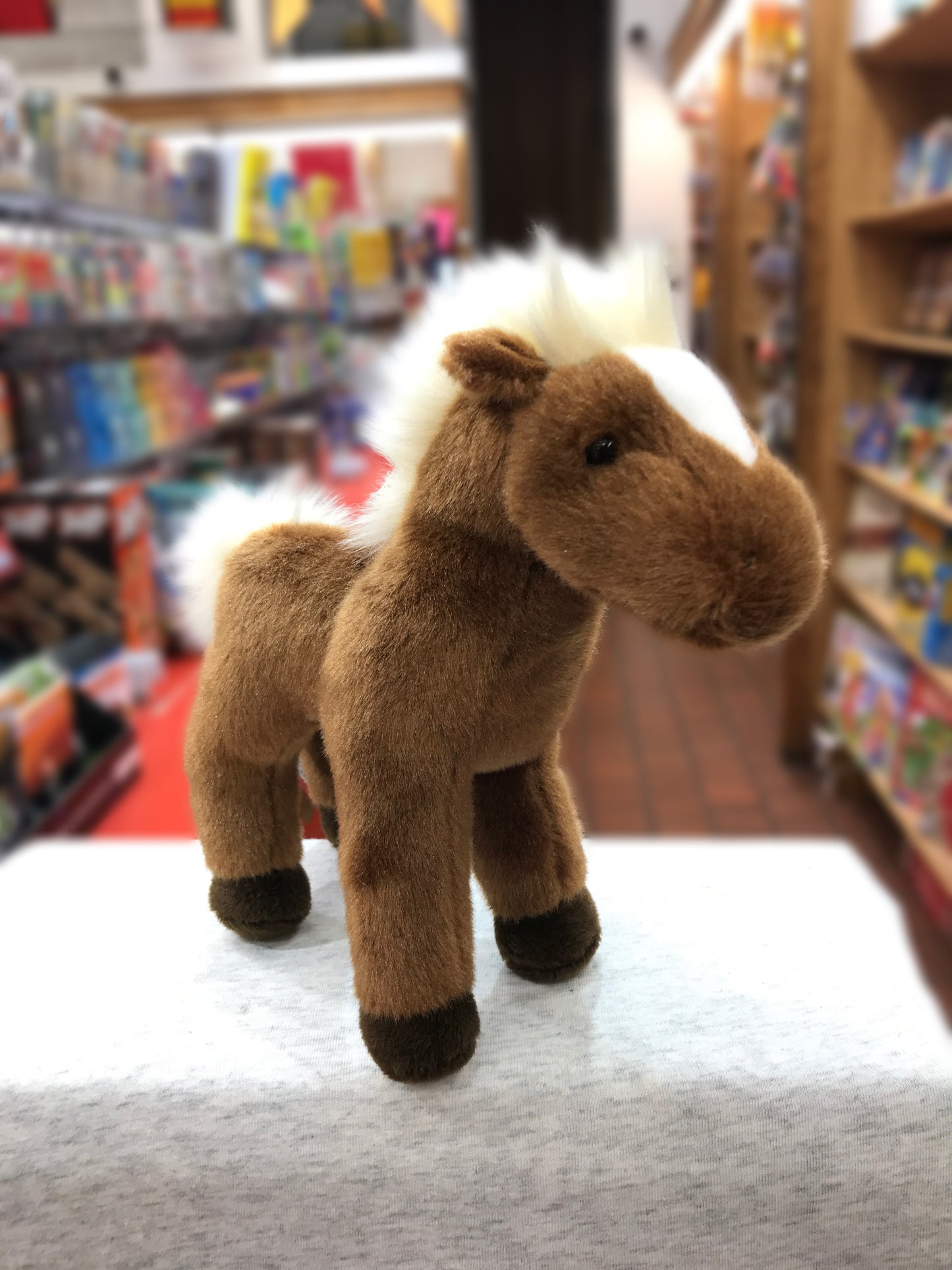 Cute chestnut horse plush toy standing on display in toy store, soft brown fur and black hooves visible