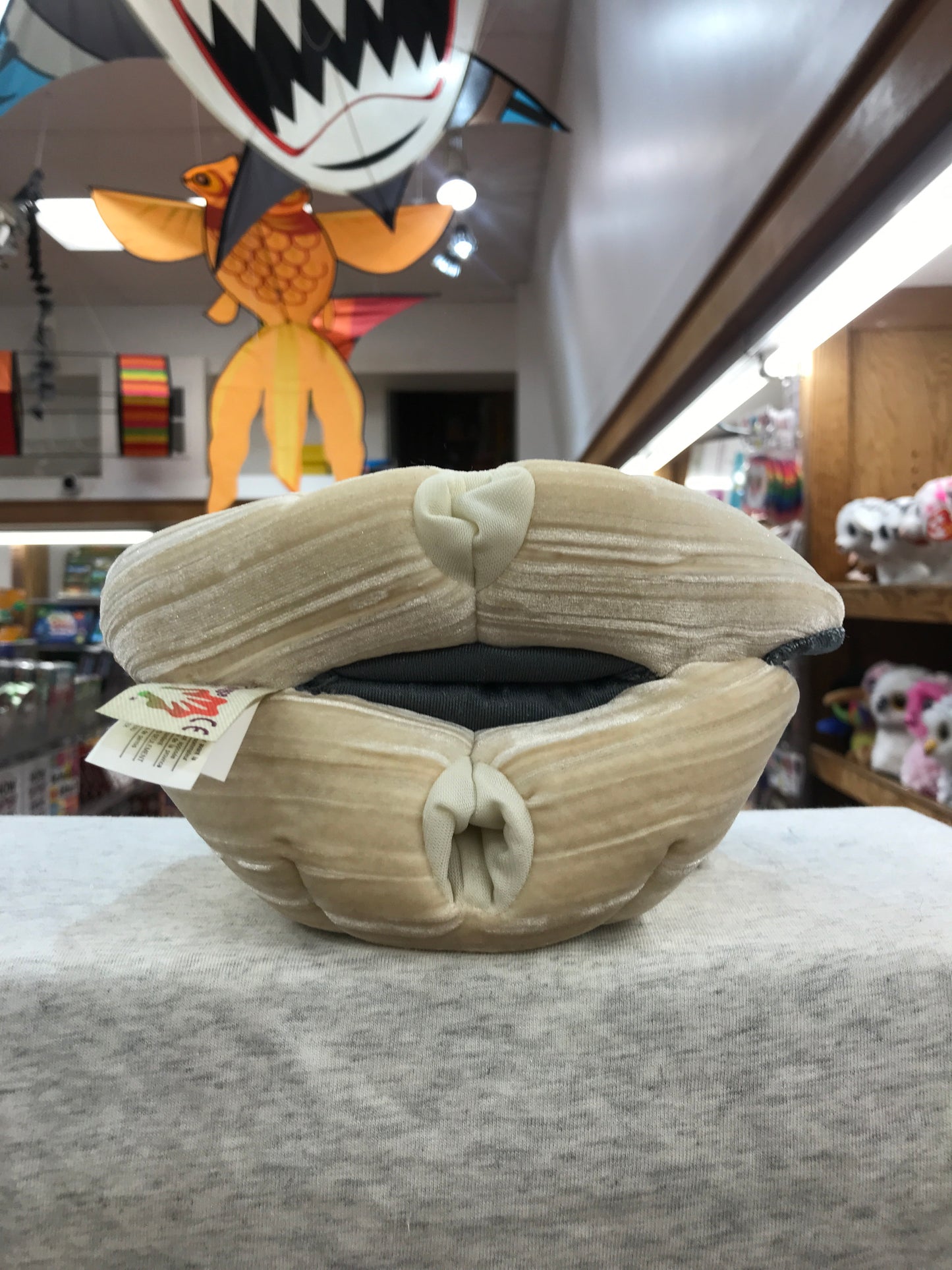 Folkmanis Giant Clam Puppet in toy store, beige plush shell with opening, colorful hanging decorations in background