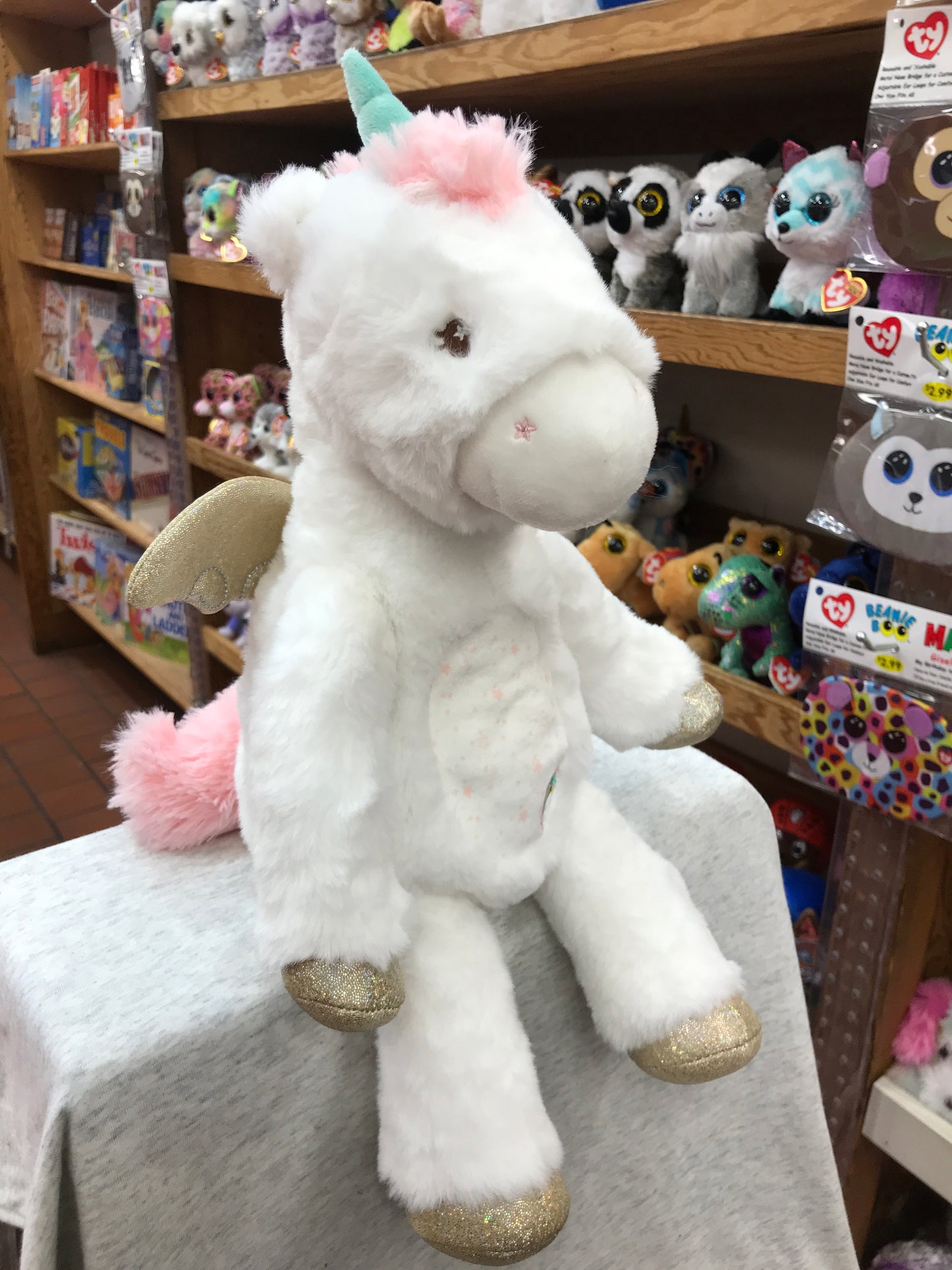 Plush unicorn Emilie with sparkly hooves, pastel horn, and wings on display in toy store among other stuffed animals
