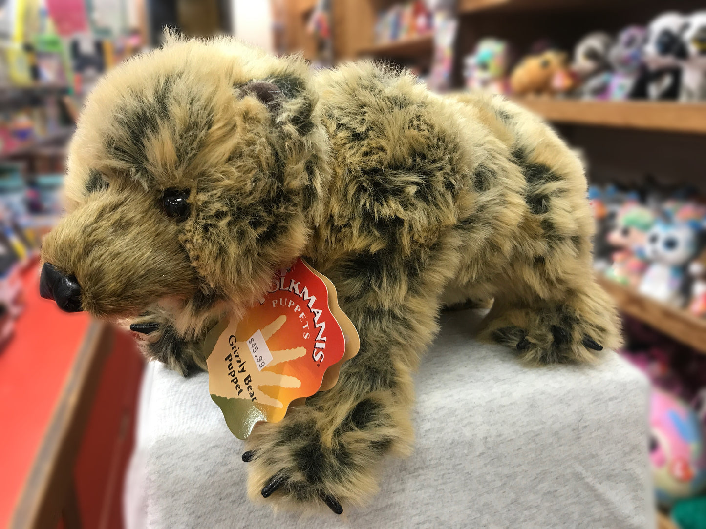 Folkmanis Grizzly Bear puppet with soft gold-tipped plush, movable mouth, and claws, displayed in a toy store with product tag
