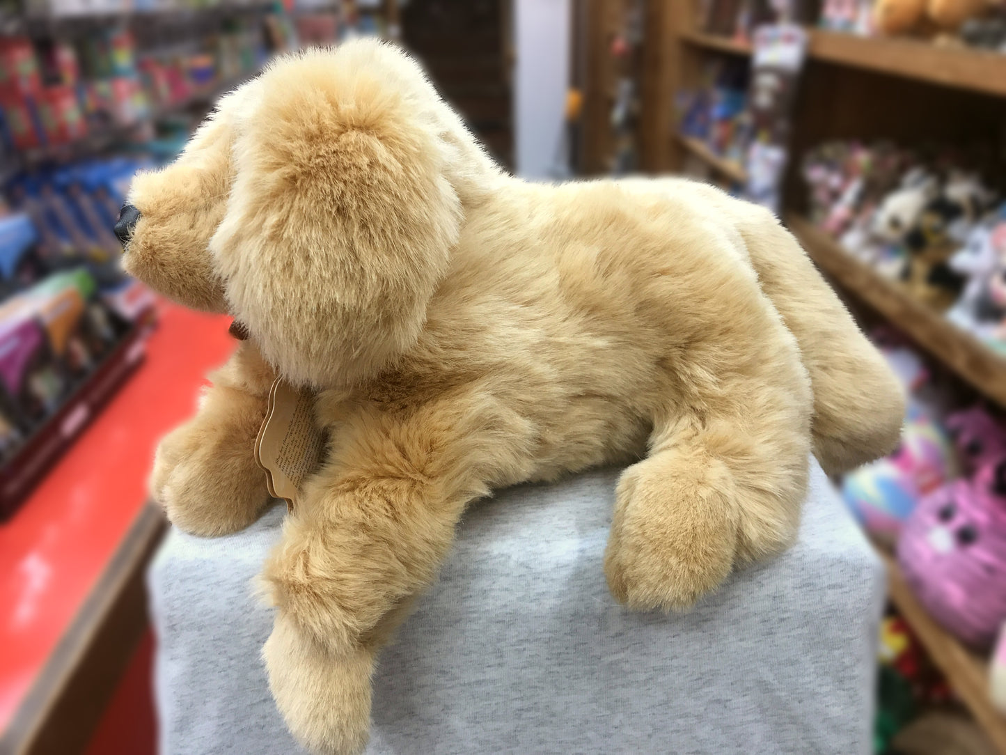 Lifelike Golden Retriever puppy puppet with soft plush fur, displayed in a toy store on a gray surface