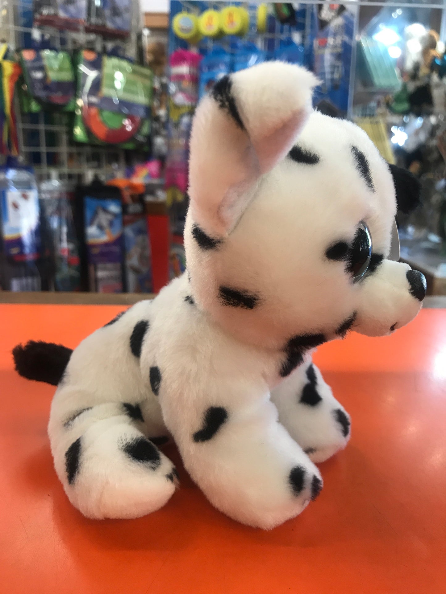 Adorable TY Beanie Boo Dalmatian plush toy sitting on orange surface, surrounded by colorful toys in store display