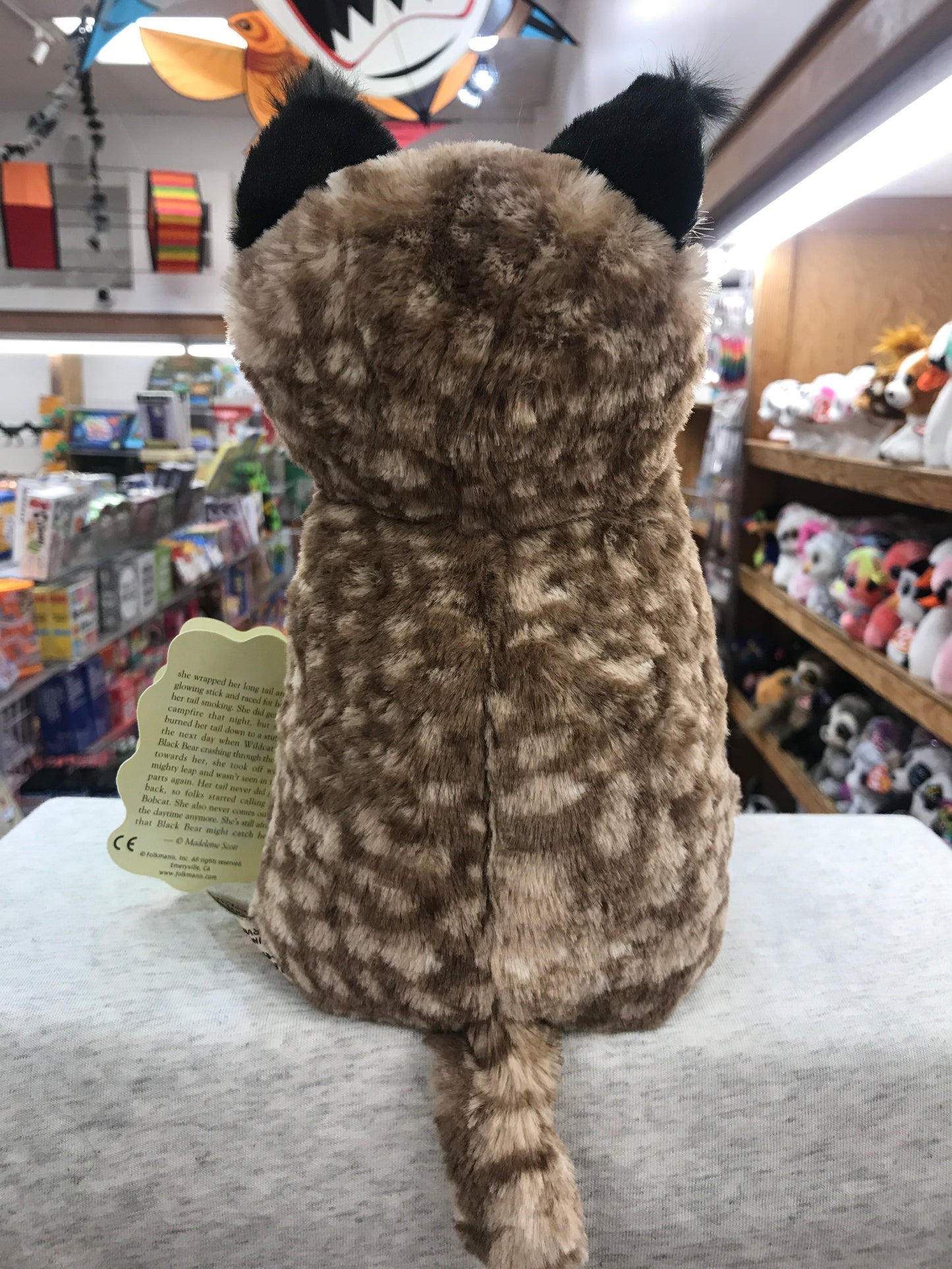 Folkmanis Bobcat Kitten puppet in toy store, brown spotted plush with black ears and tail, viewed from behind