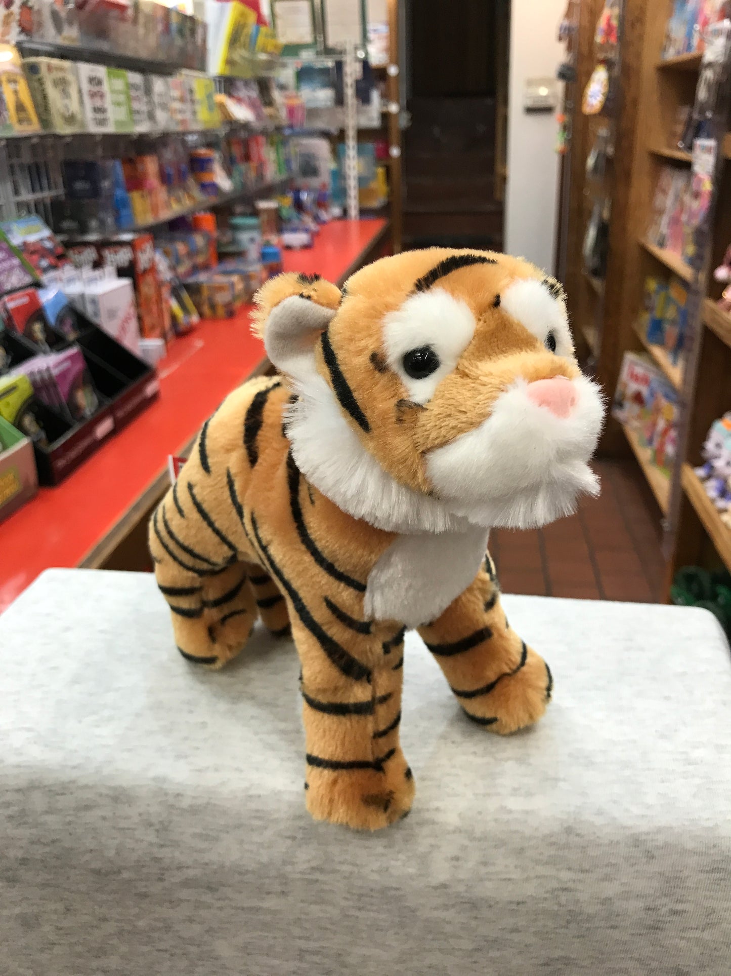 Adorable Douglas Lava Tiger plush toy standing on display in toy store, with realistic orange and black striped fur and white facial markings