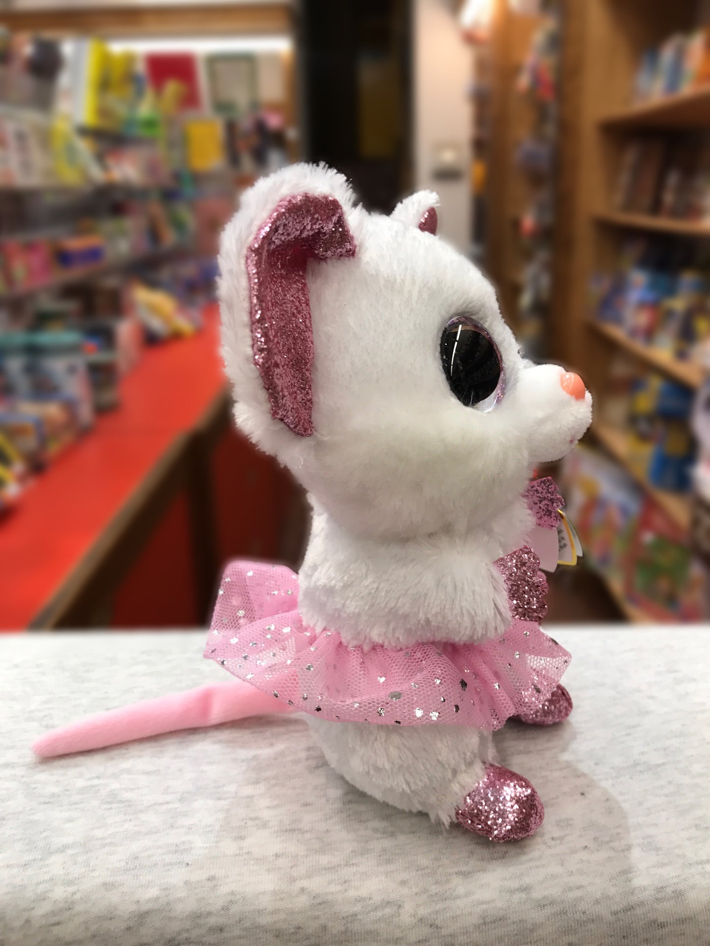 Ty Beanie Boo Nina white mouse plush wearing pink sparkly tutu, displayed in toy store with large eyes and glittery ears