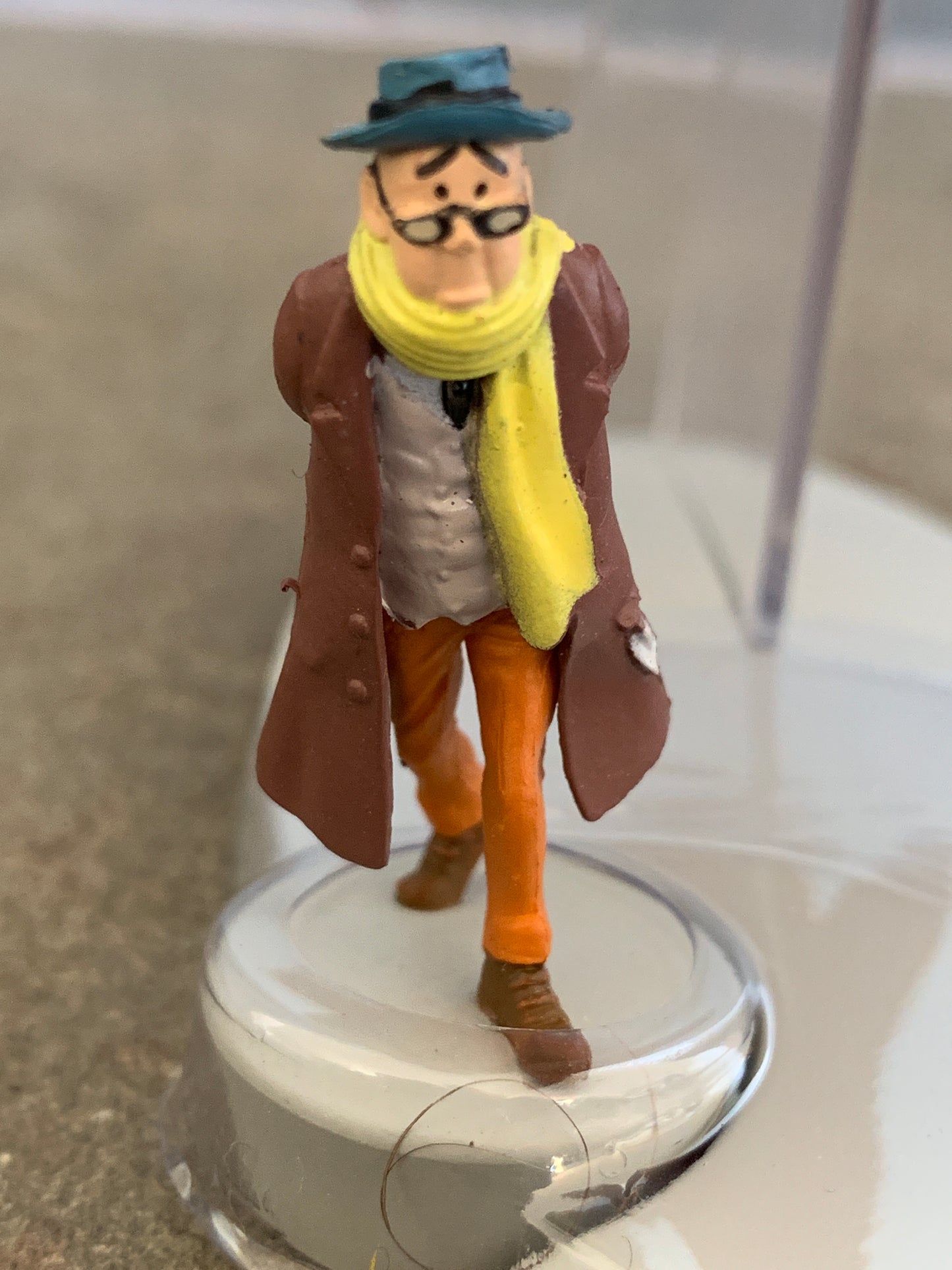 Miniature figurine of Carreidas character from Flight 714, wearing distinctive hat, scarf, and coat, on display stand
