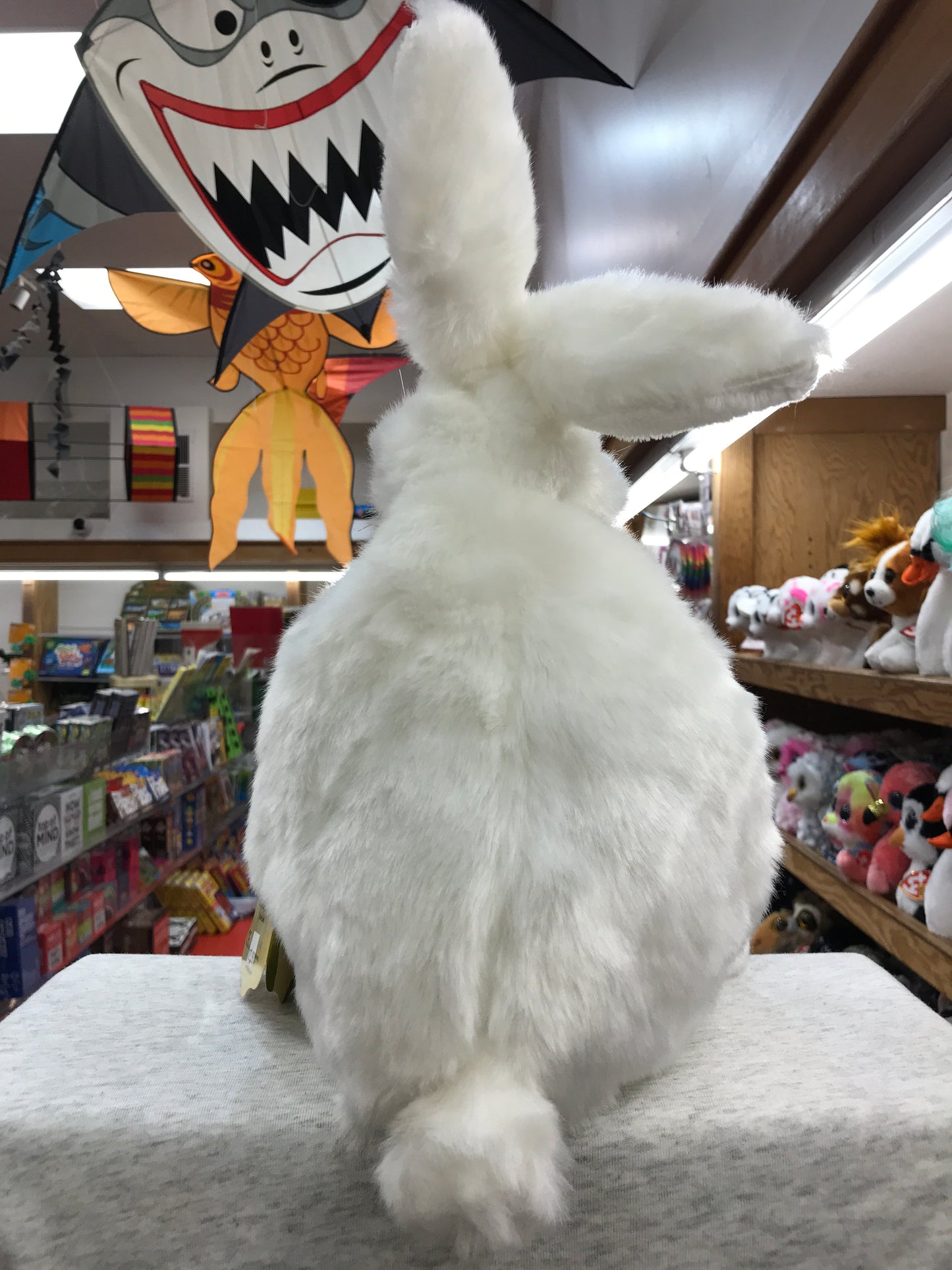 Large white rabbit puppet standing in toy store, surrounded by colorful toys and decorations, showcasing its soft fur and size