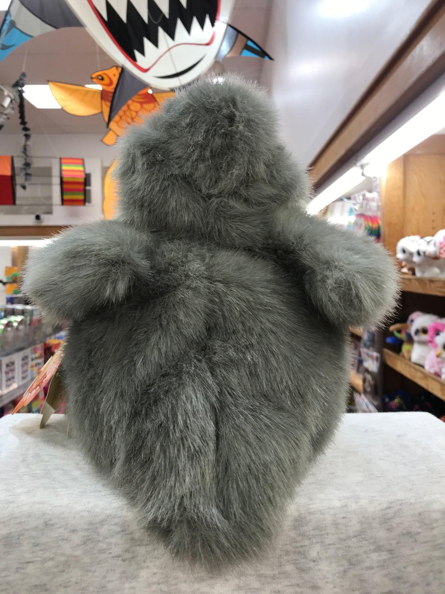 Plush gray Folkmanis baby swan puppet in toy store, viewed from back showing fluffy body and wings