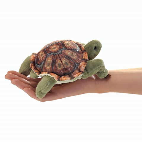 Folkmanis Mini Tortoise finger puppet with retractable head, shown on palm for size reference. Plush green body, detailed shell.