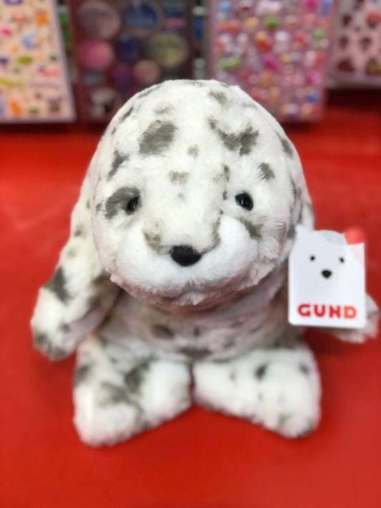Gund Nuri leopard seal plush toy with white and gray spotted design, sitting on red surface with tag visible