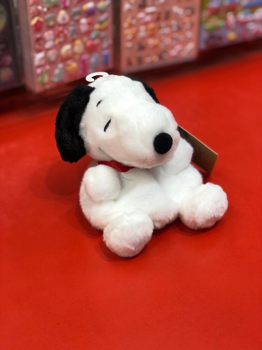Adorable Peanuts Snoopy plush toy on red surface, soft white fur with black ears and red collar, part of Aurora collection