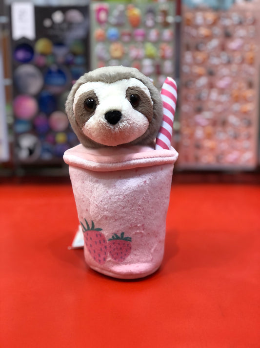 Cute sloth plush peeking out of pink smoothie cup toy, strawberry design, colorful toy displays in background