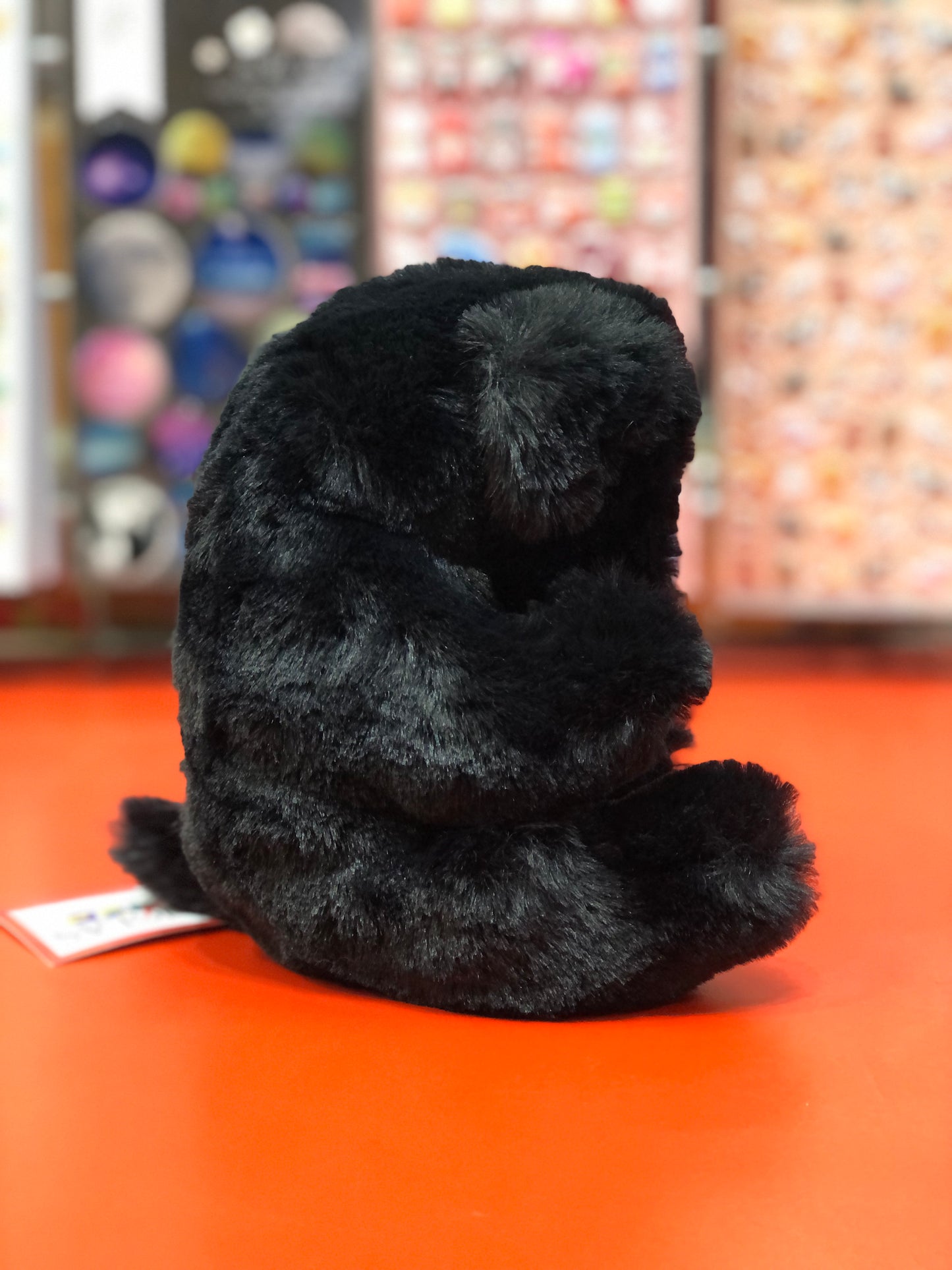 Soft, plush black Labrador puppy toy lying on its back, showcasing fluffy fur and cute pose on orange surface