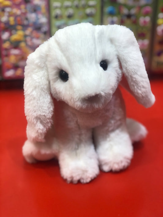 Soft white bunny plush toy with long floppy ears and big dark eyes, sitting on red surface against colorful background
