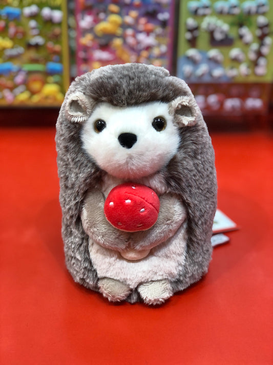 Adorable Stuey hedgehog plush toy holding red mushroom, soft brown and white fur, on red surface with colorful background