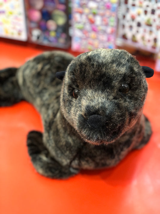 Realistic sea lion plush toy on red surface, close-up of soft furry face and body, colorful background